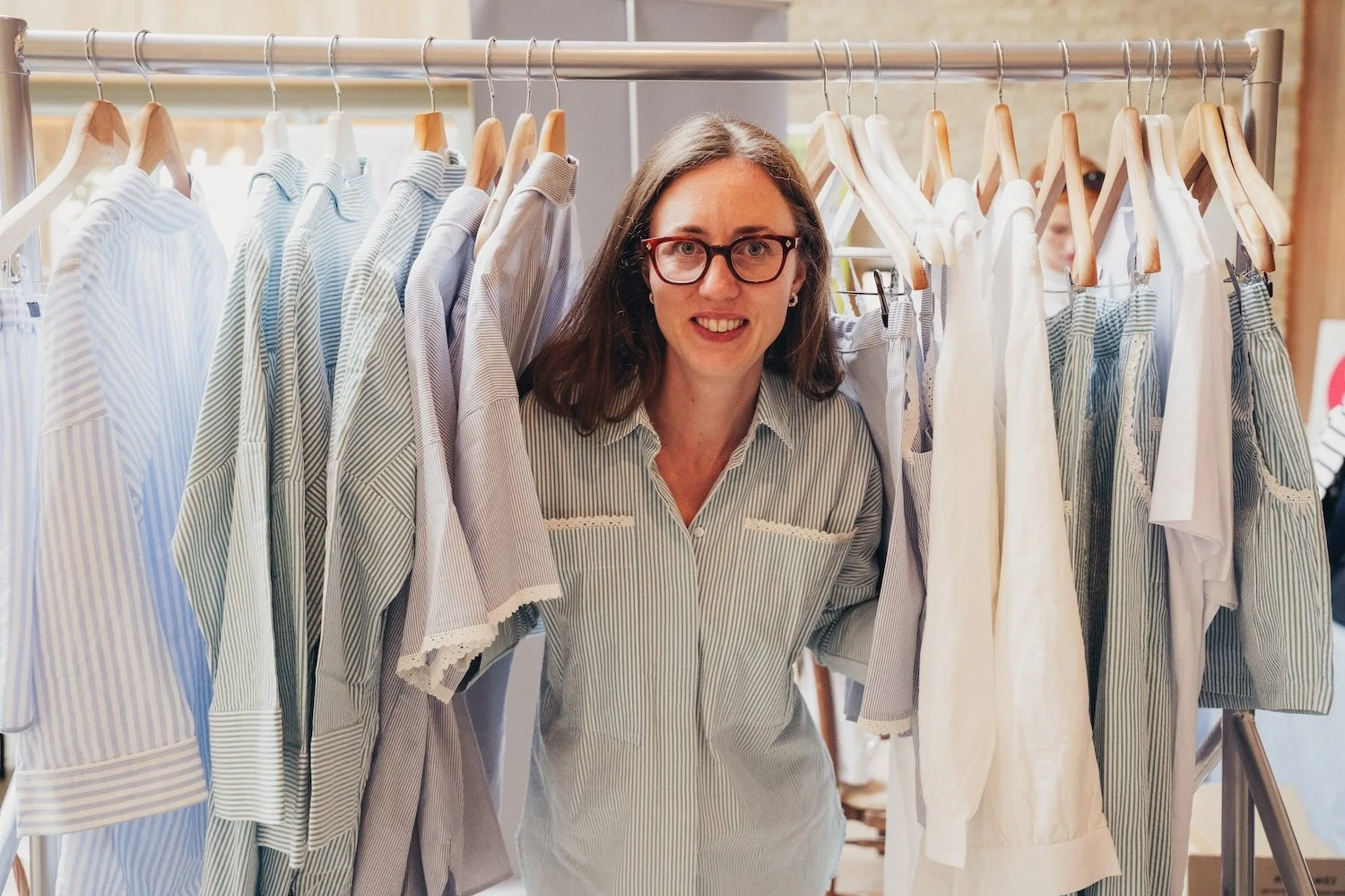 A woman with glasses stands behind a clothing rack filled with striped PJs - shopping at at a She's Electric event