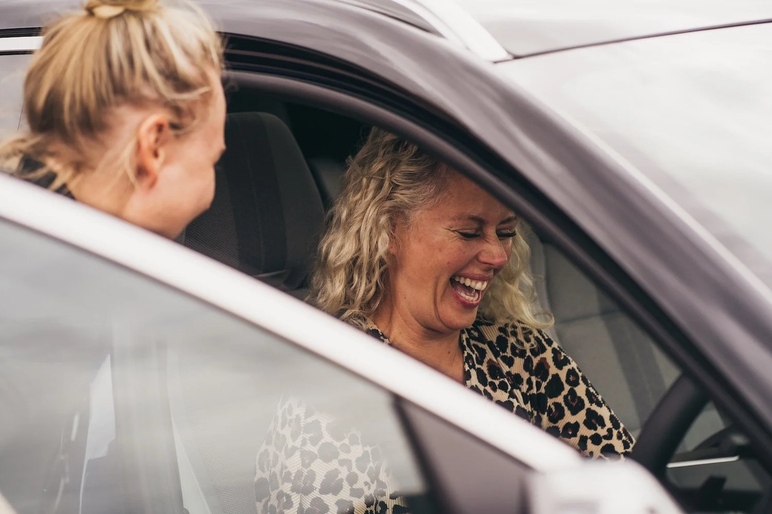Two women inside an ev, one is sitting in the driver's seat and the other in the passenger seat, both laughing