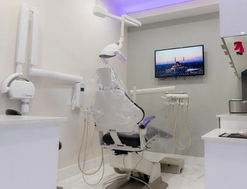 Dental examination room with a dental chair covered in plastic, dental equipment, and a mounted TV screen showing a cityscape.