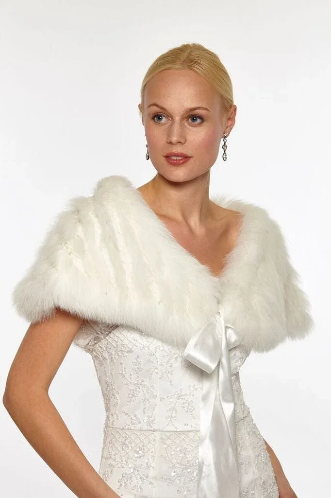 A woman with blonde hair, wearing wedding attire including a white satin dress with lace details, a white fur shawl, and dangling earrings.