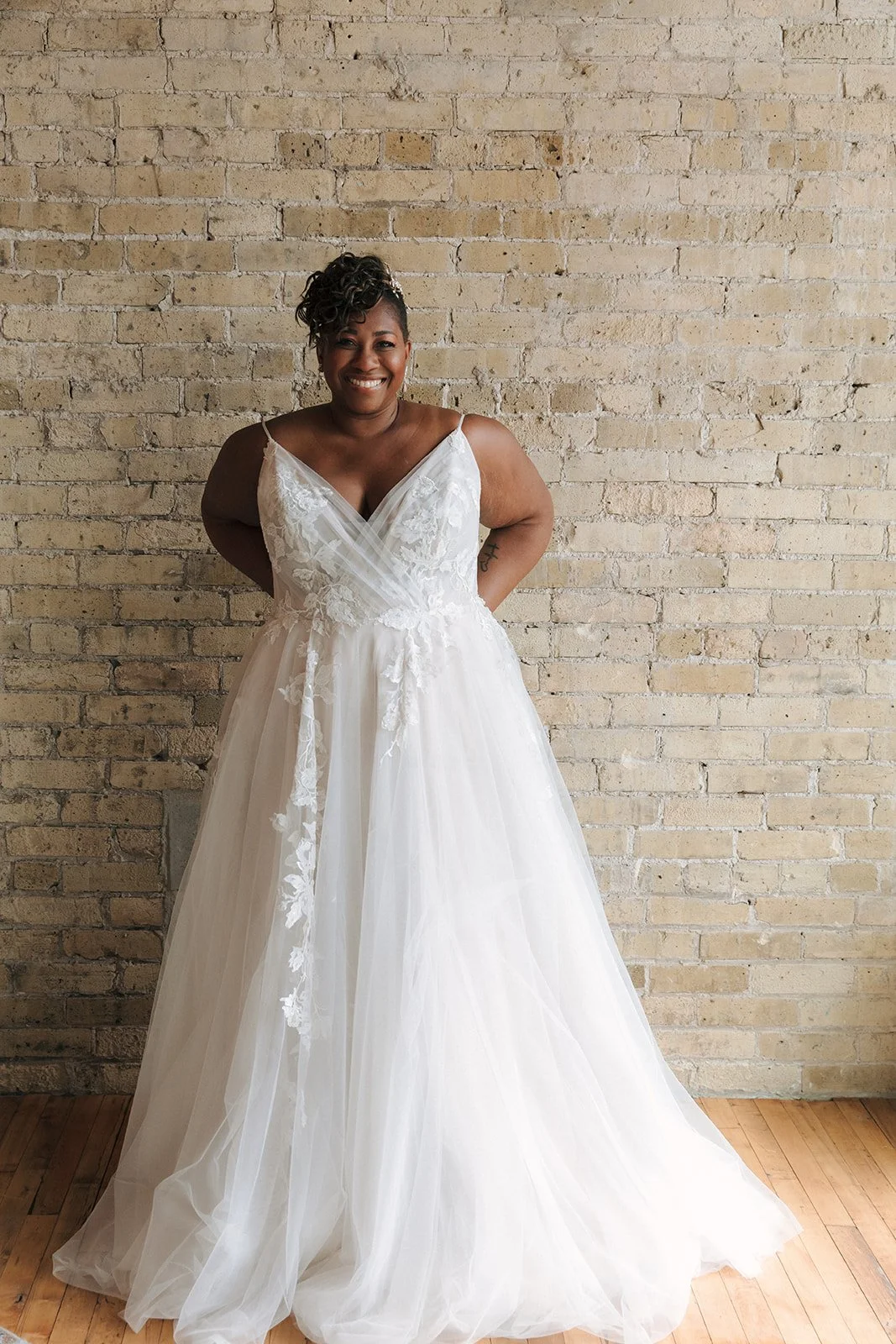 A woman in a white wedding dress smiling in front of a brick wall.