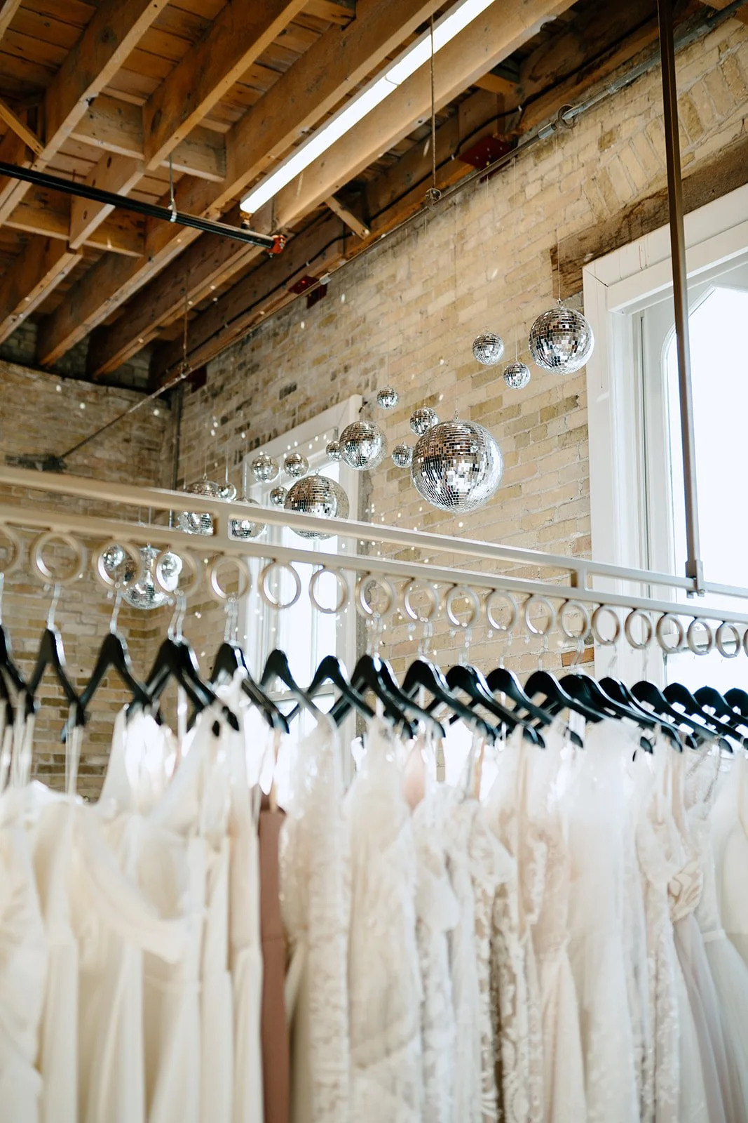 Clothing store with wedding dresses hanging on a rack, and disco balls of varying sizes hanging from the ceiling.