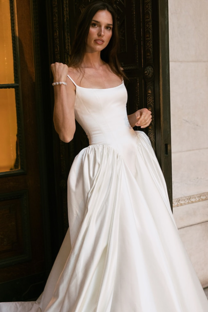 bride wearing a wedding dress with basque waist and spaghetti straps leaning against the wall