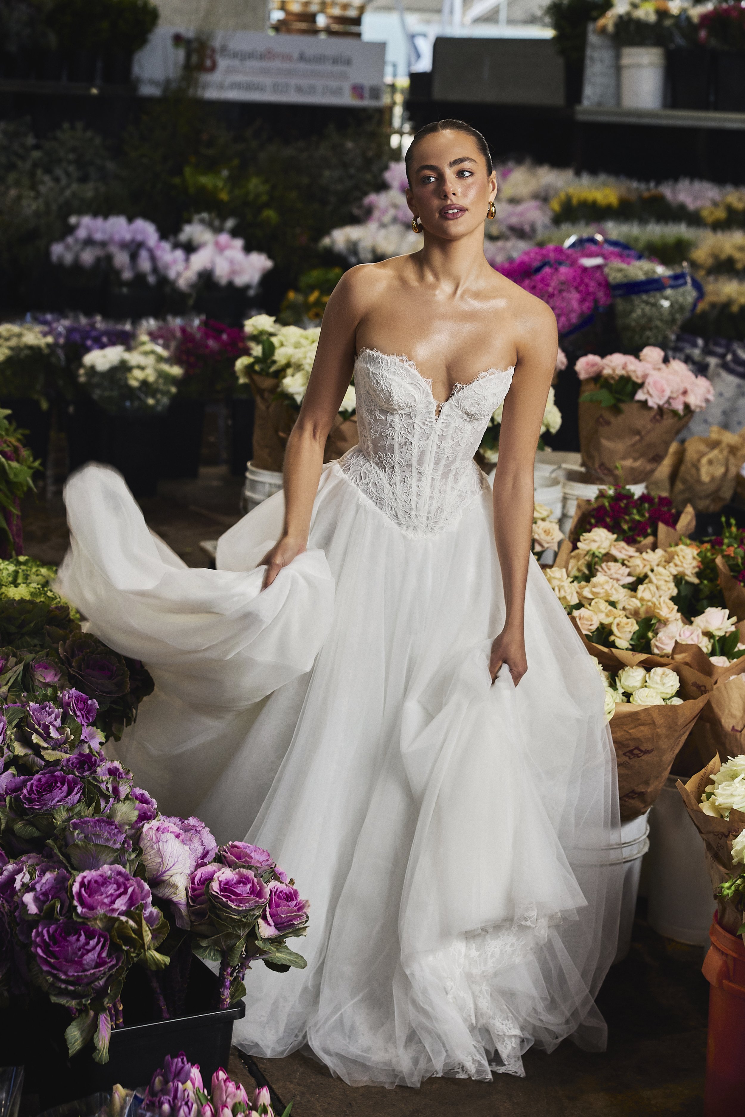 A young woman in a white wedding dress standing among a display of colorful flowers at a flower market.
