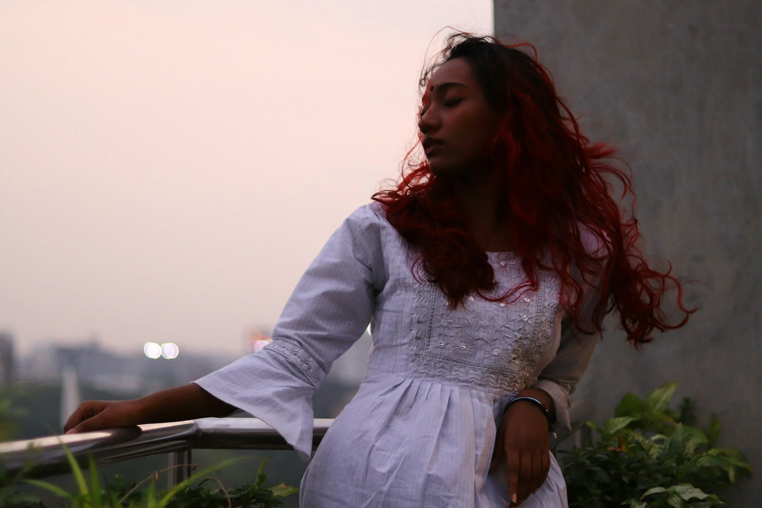 Woman standing on a balcony at sunset with the wind in her hair, reflecting a moment of freedom and calm that symbolizes reaching a new level of release and empowerment in OCD recovery.