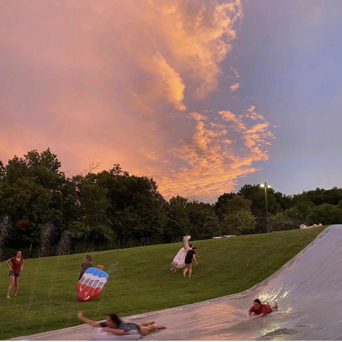 beautiful sunset over mega slip and slide. young adults are climbing the hill to slide down again