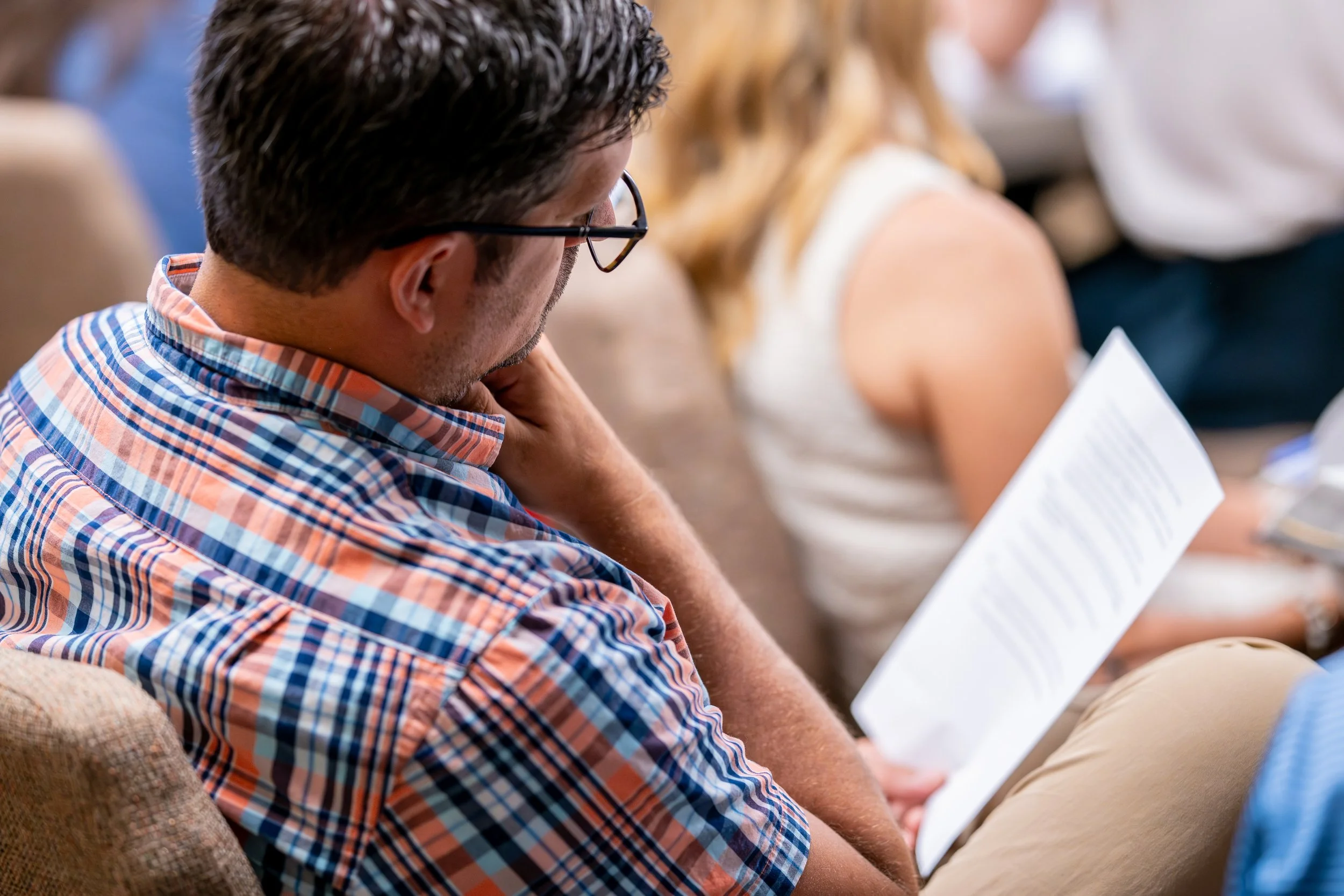 A man with dark hair, wearing glasses and a plaid shirt, reading the bulletin during a worship service at West End Community Church in Nashville, TN.