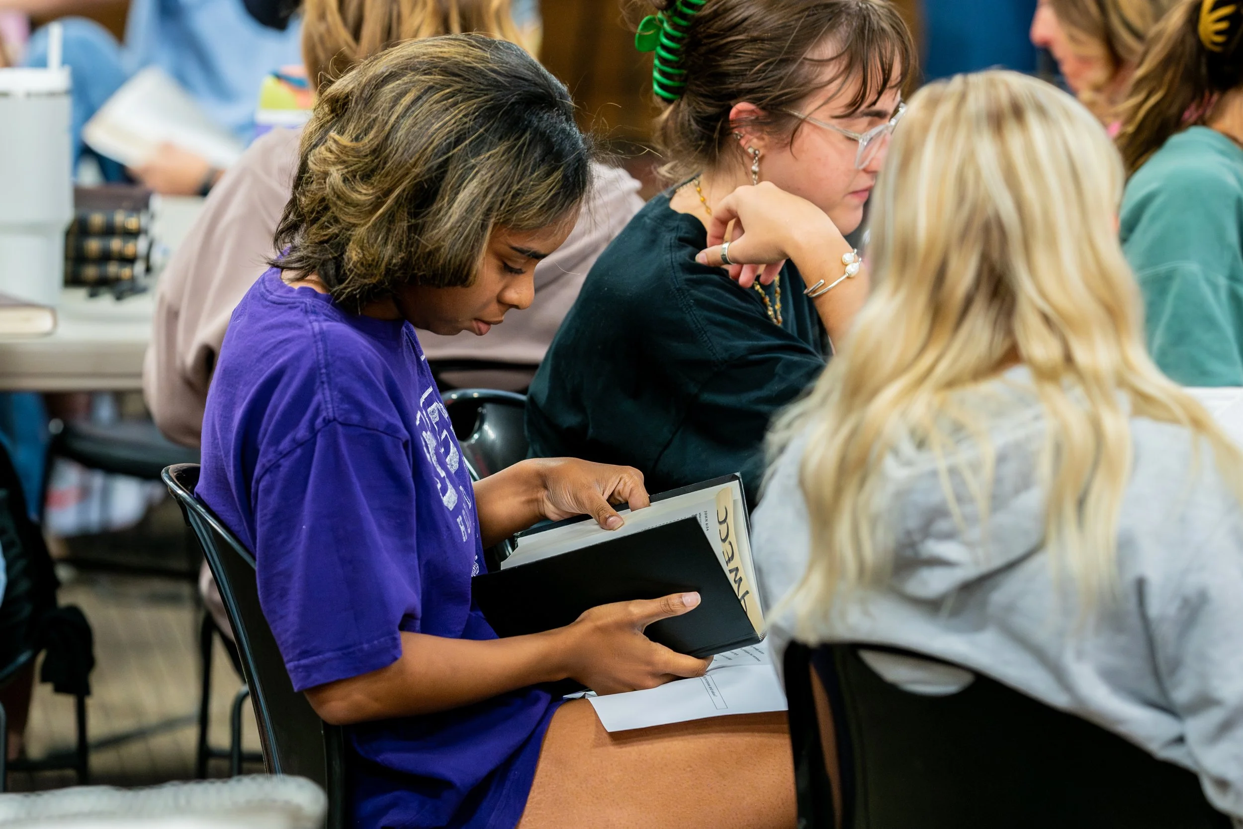 girl reading bible during bible study. others listening to speaker