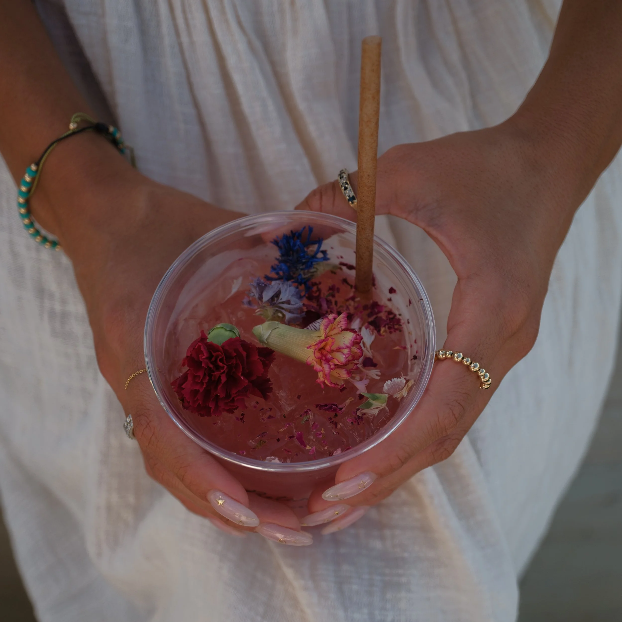 A woman’s hands holding a disposable plastic cup full of a mocktail with edible flowers and edible rose petals