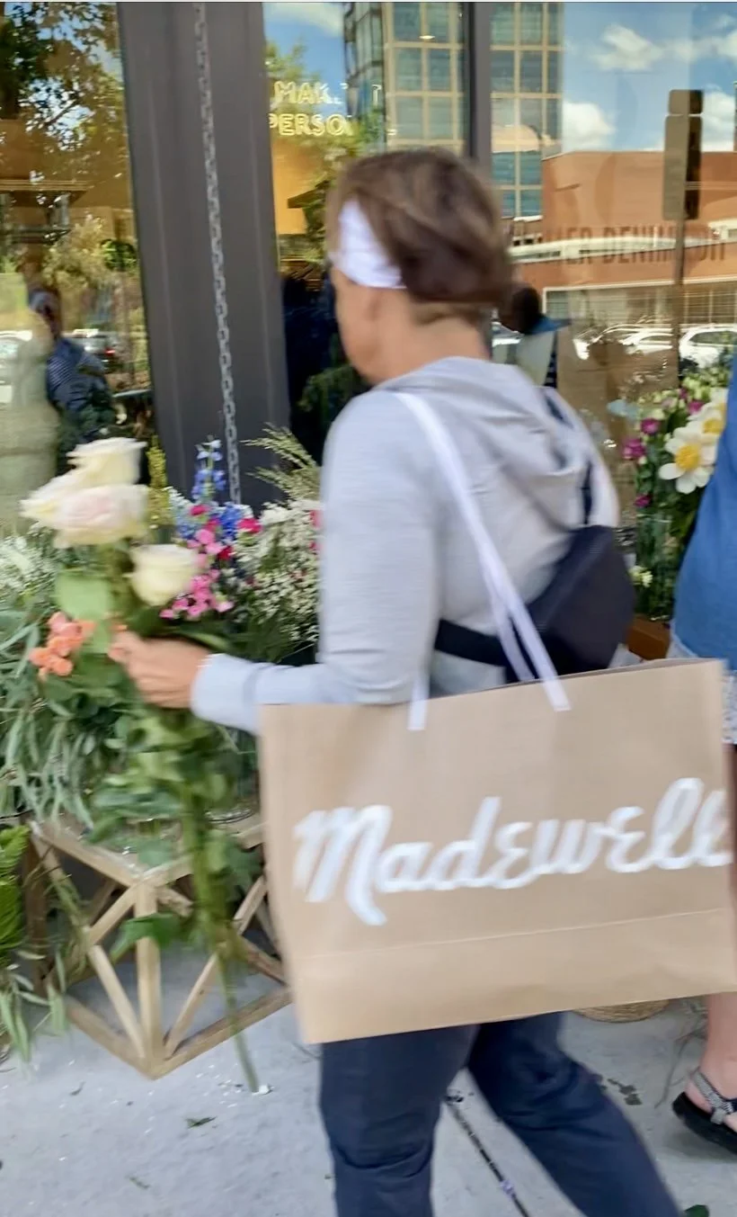 A women picking out flowers from a flower bar in Charlotte, NC outside of a Madewell store with a Madewell shopping bag