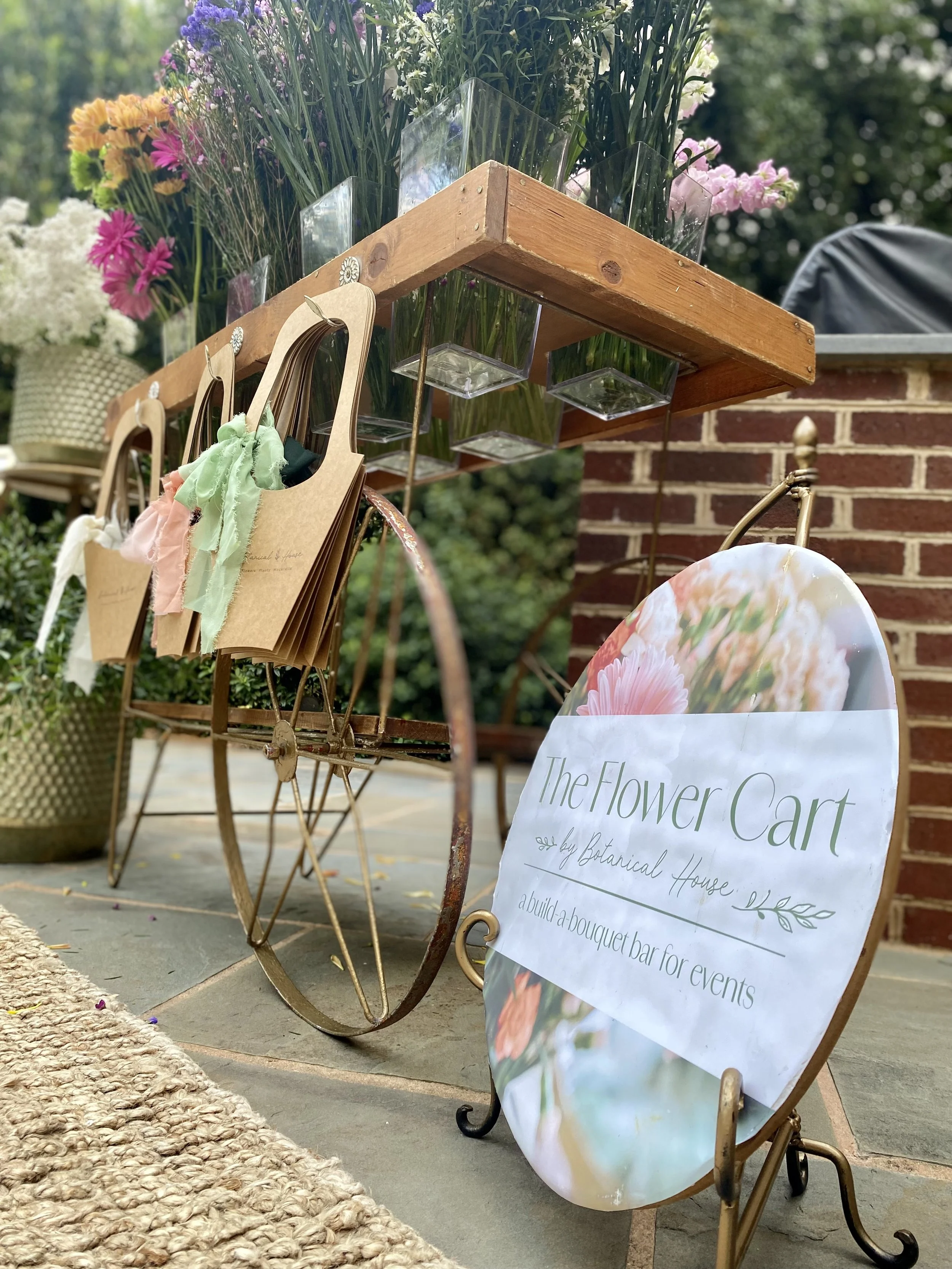 a picture of a sign that says "the flower cart" next to a small flower cart stocked with fresh colorful flowers and with bouquet holders handing on the front