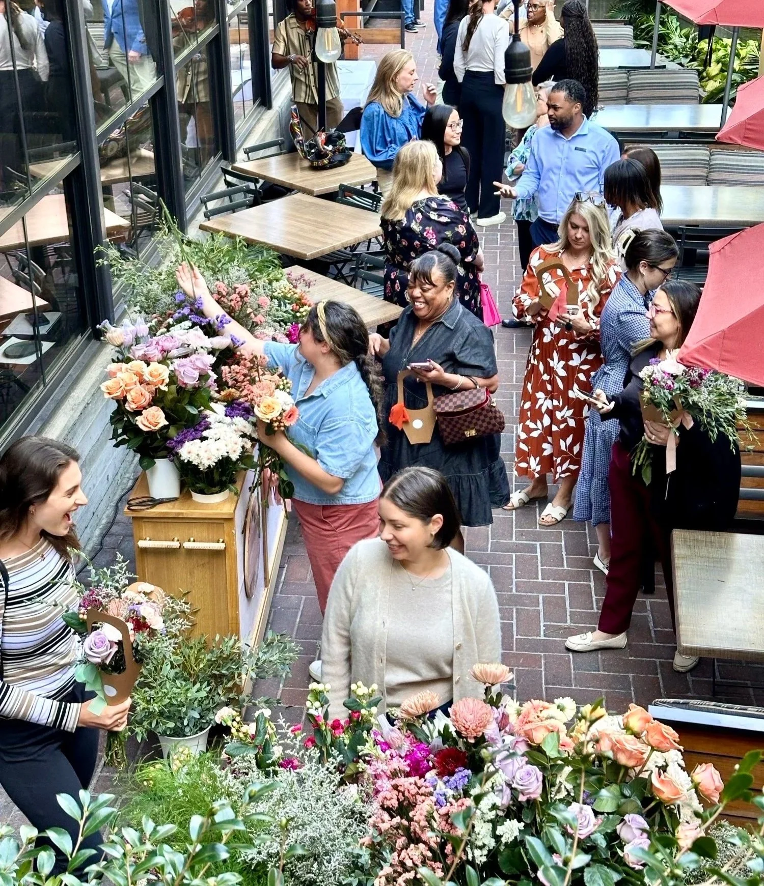 guests at an outdoor event on a restaurant patio surrounding a flower cart and building bouquets