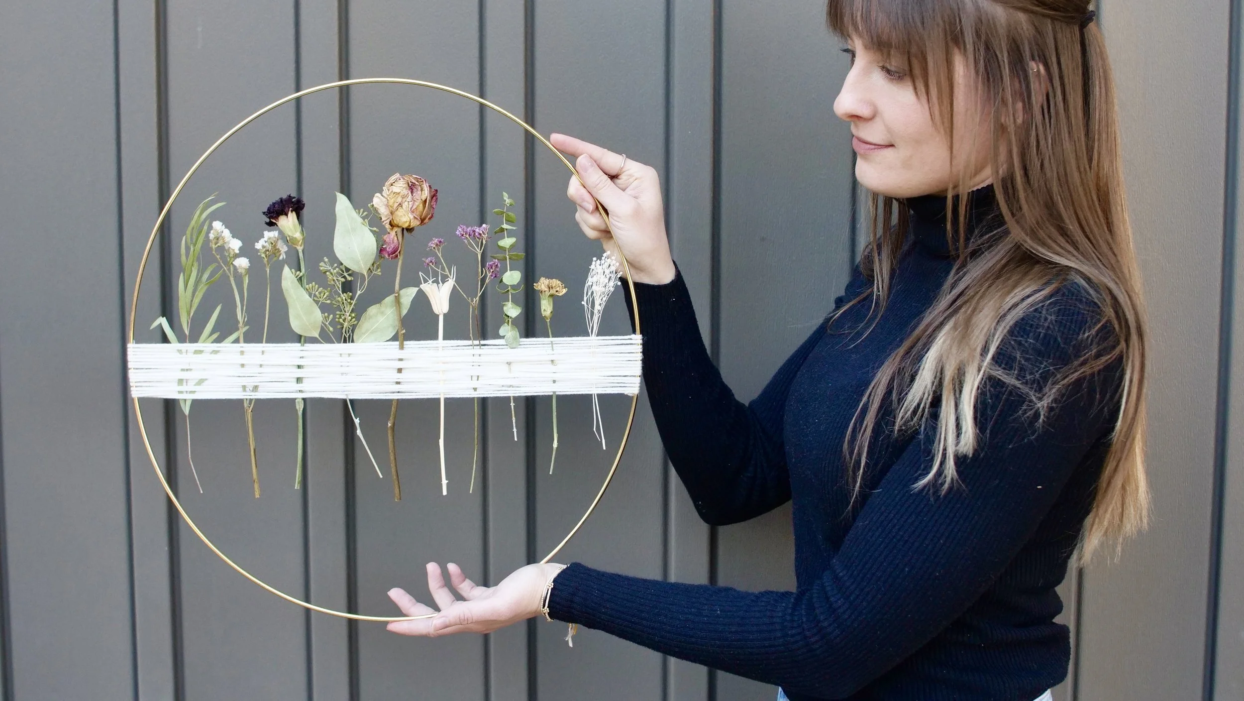 Two handing holding a macrame gold ring Boho wall decoration with dried flowers and eucalyptus woven into it