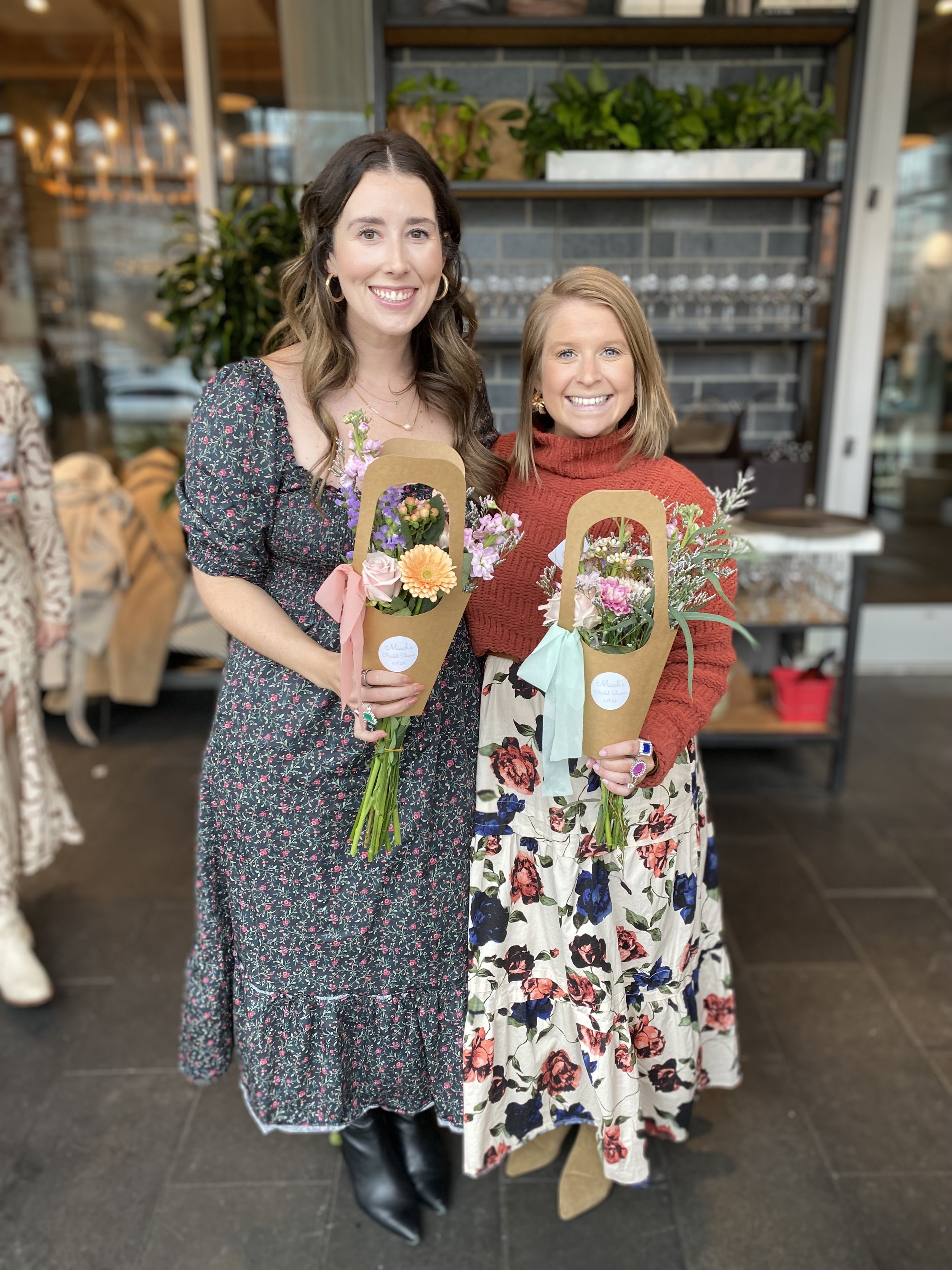 two women smiling and holding bouquets of flowers