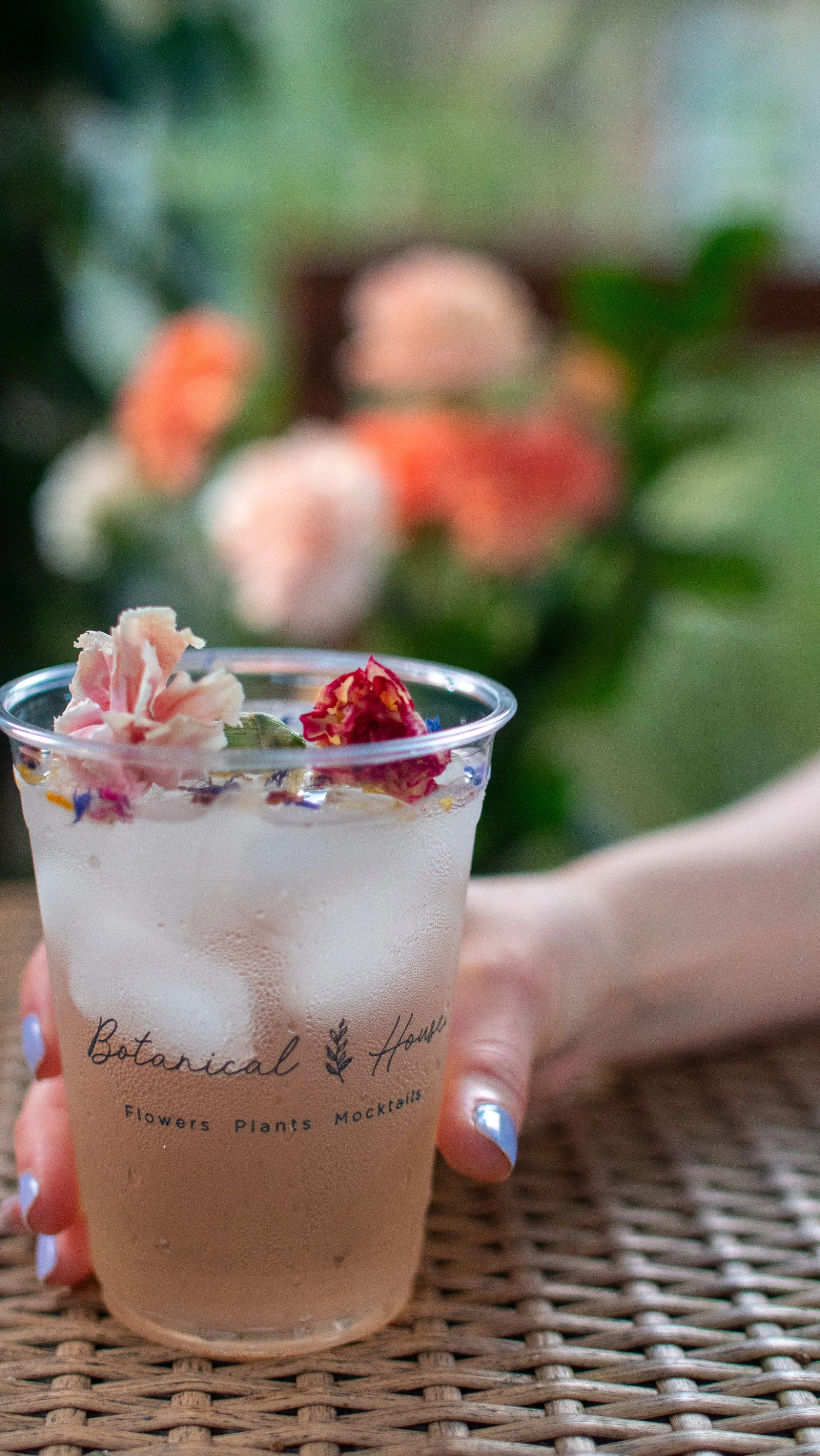A hand holding a mocktail drink with edible flowers