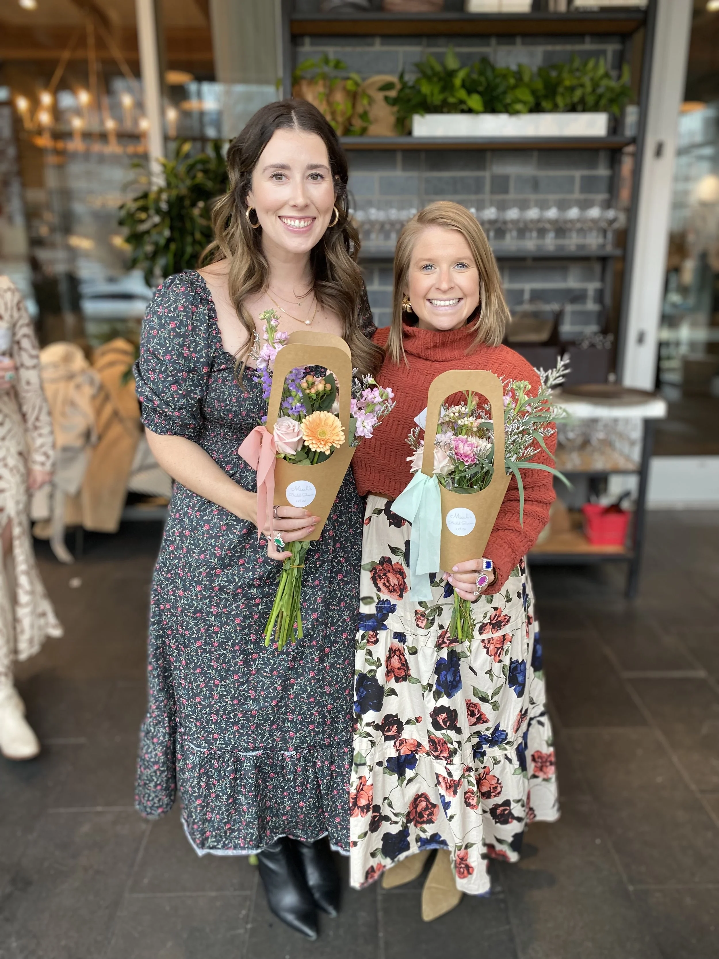 Two women smiling holding bouquets of flowers they made