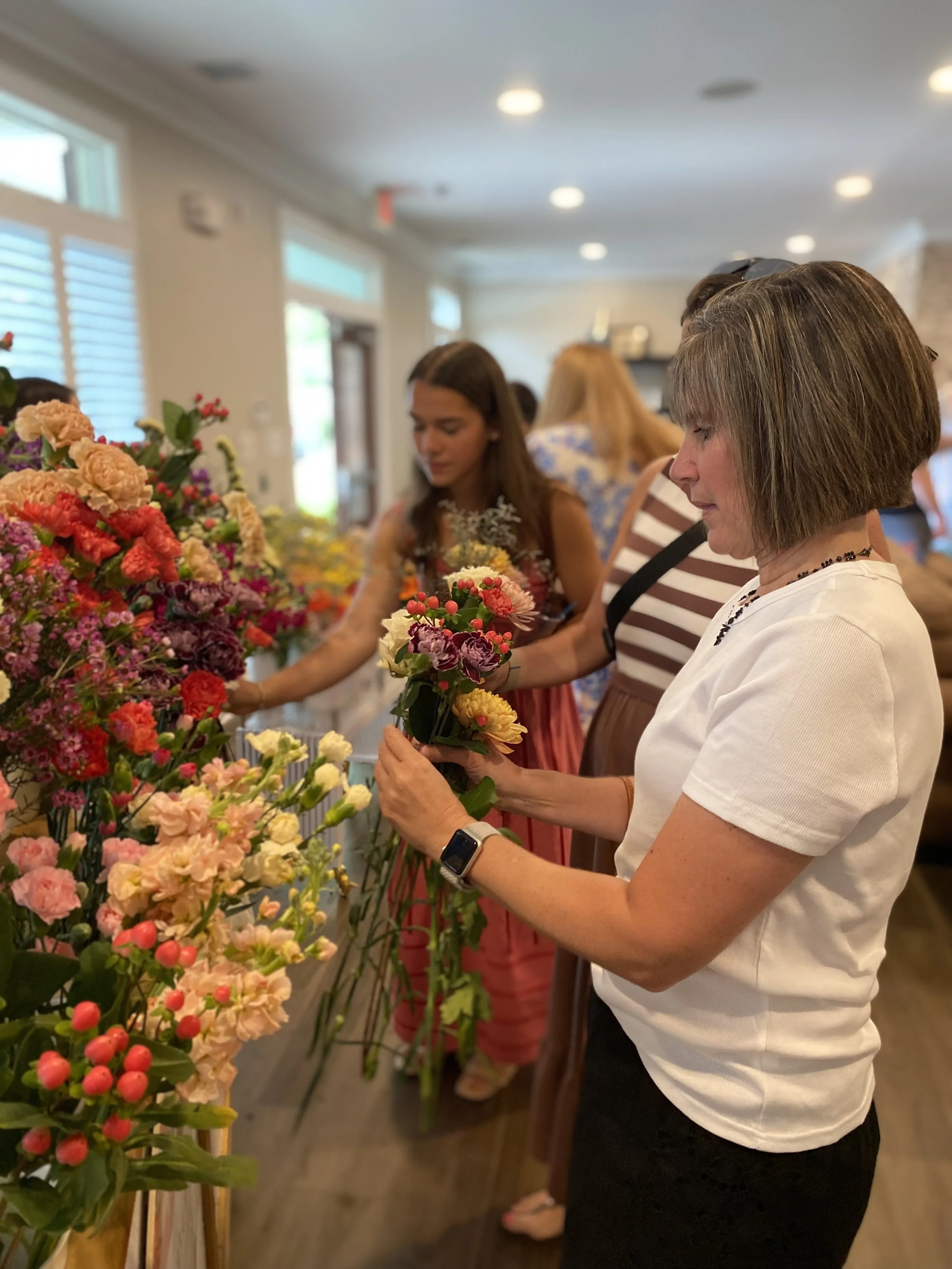 a women building a bouquet at a flower cart indoors with women in the background
