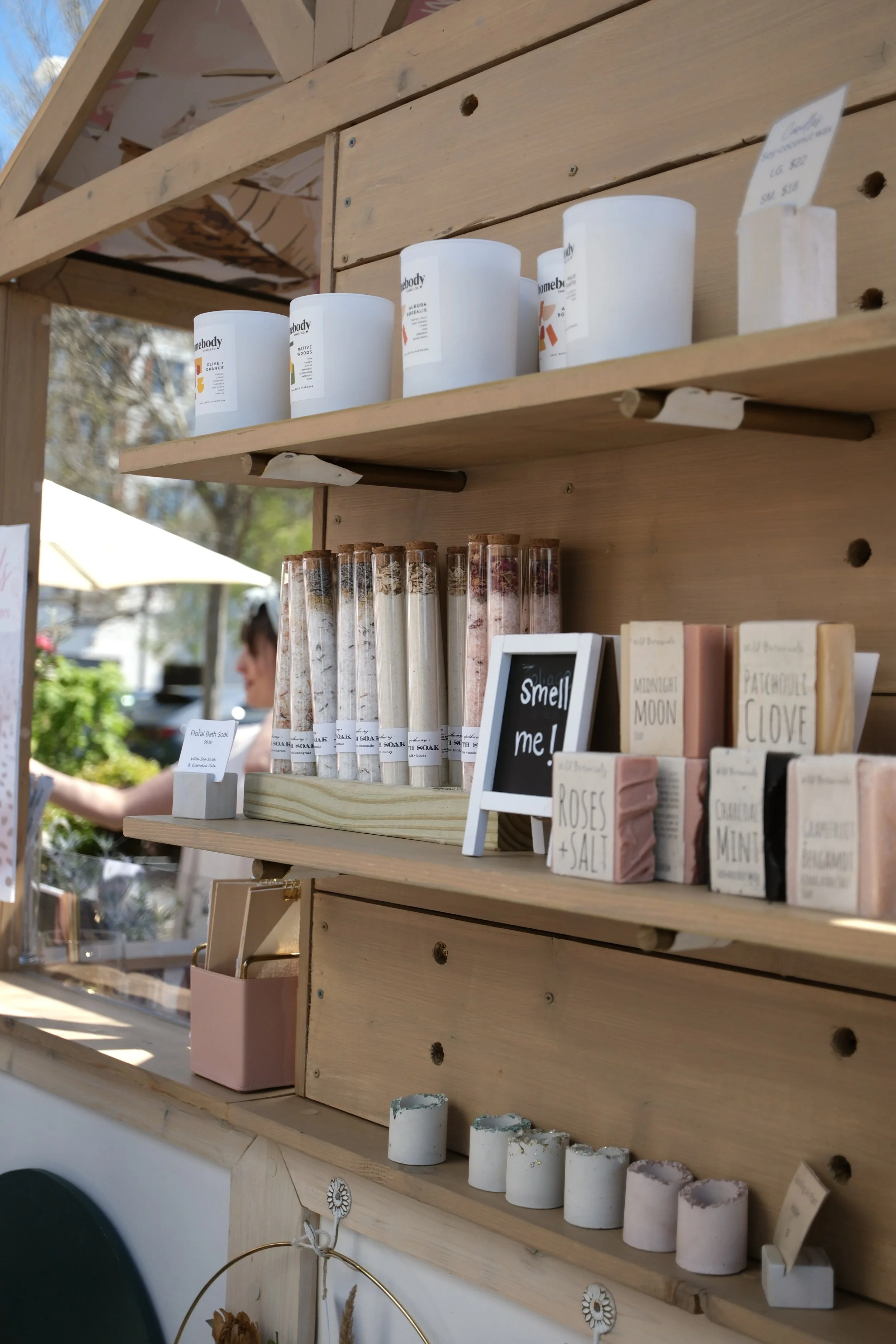 Shelves on an outdoor market cart full of products like bath salts, candles, and soaps