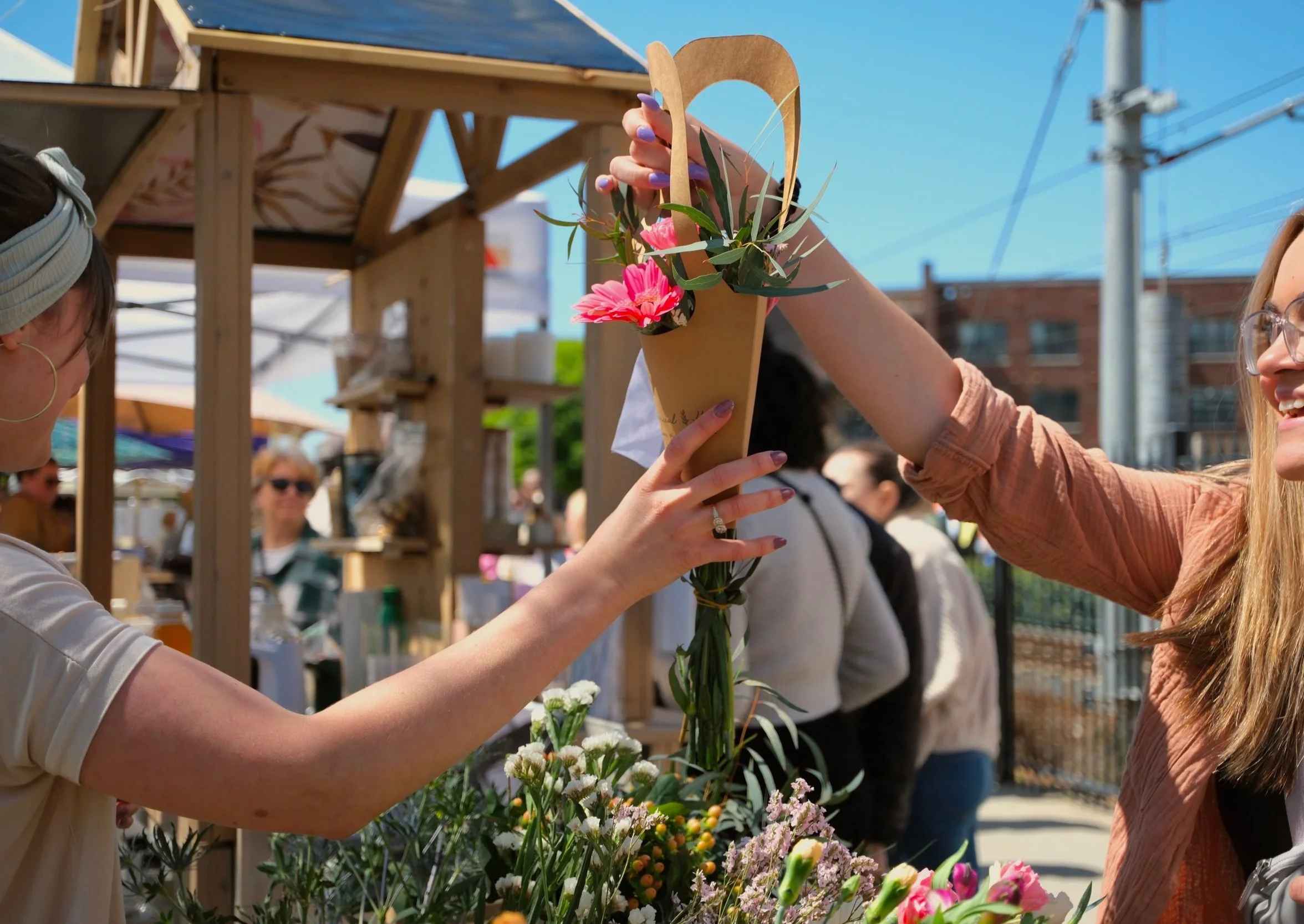 Someone handing a women a bouquet of flowers in a paper flower bag from a build your own bouquet cart