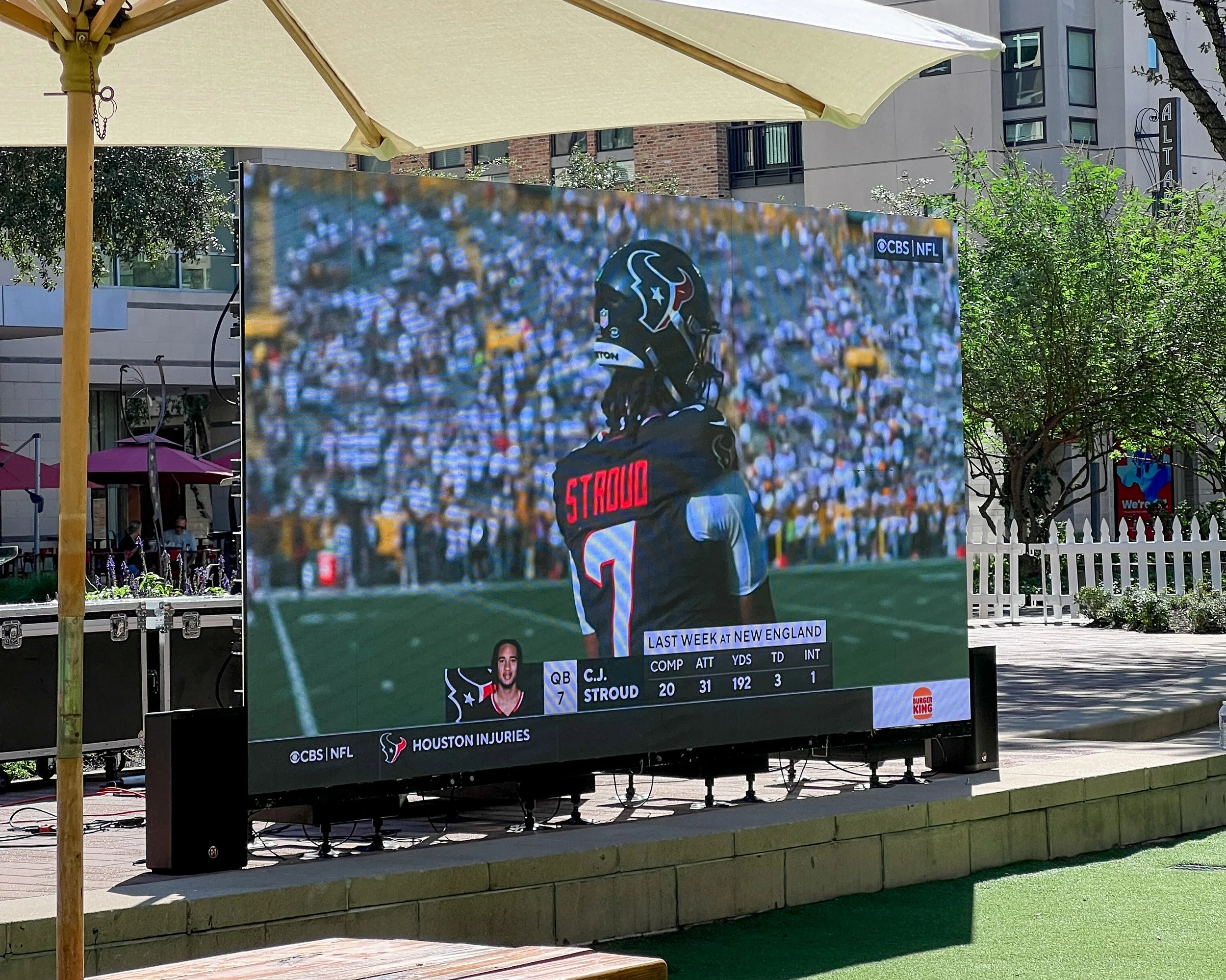 Large outdoor digital screen displaying a football player in uniform with the name 'Stroud' on the back, standing on a football field with a large crowd in the background. The screen shows player stats and information, including team and sponsor logos.