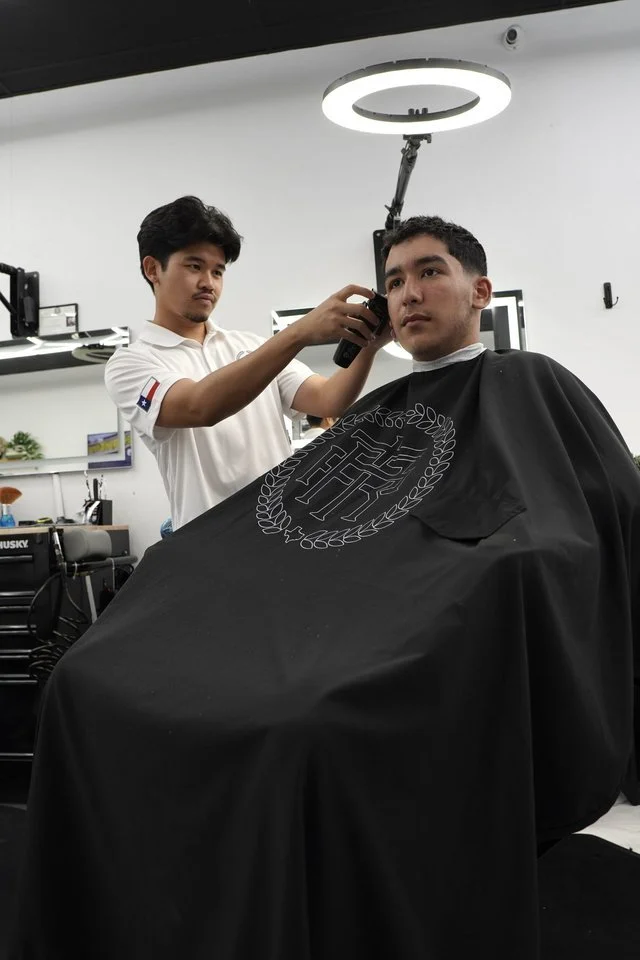 Barber at The Rooted Parlor in Sugar Land using clippers to fade a client's hair under a ring light in the shop
