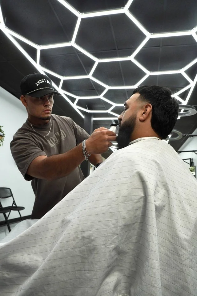 Barber at The Rooted Parlor Sugar Land barbershop trimming a client's beard with electric trimmers under the shop's honeycomb lights