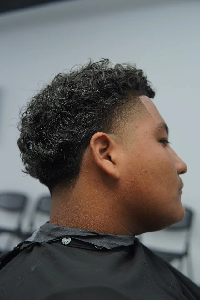 Fresh mid-taper fade on curly hair finished in the chair at The Rooted Parlor barbershop in Sugar Land