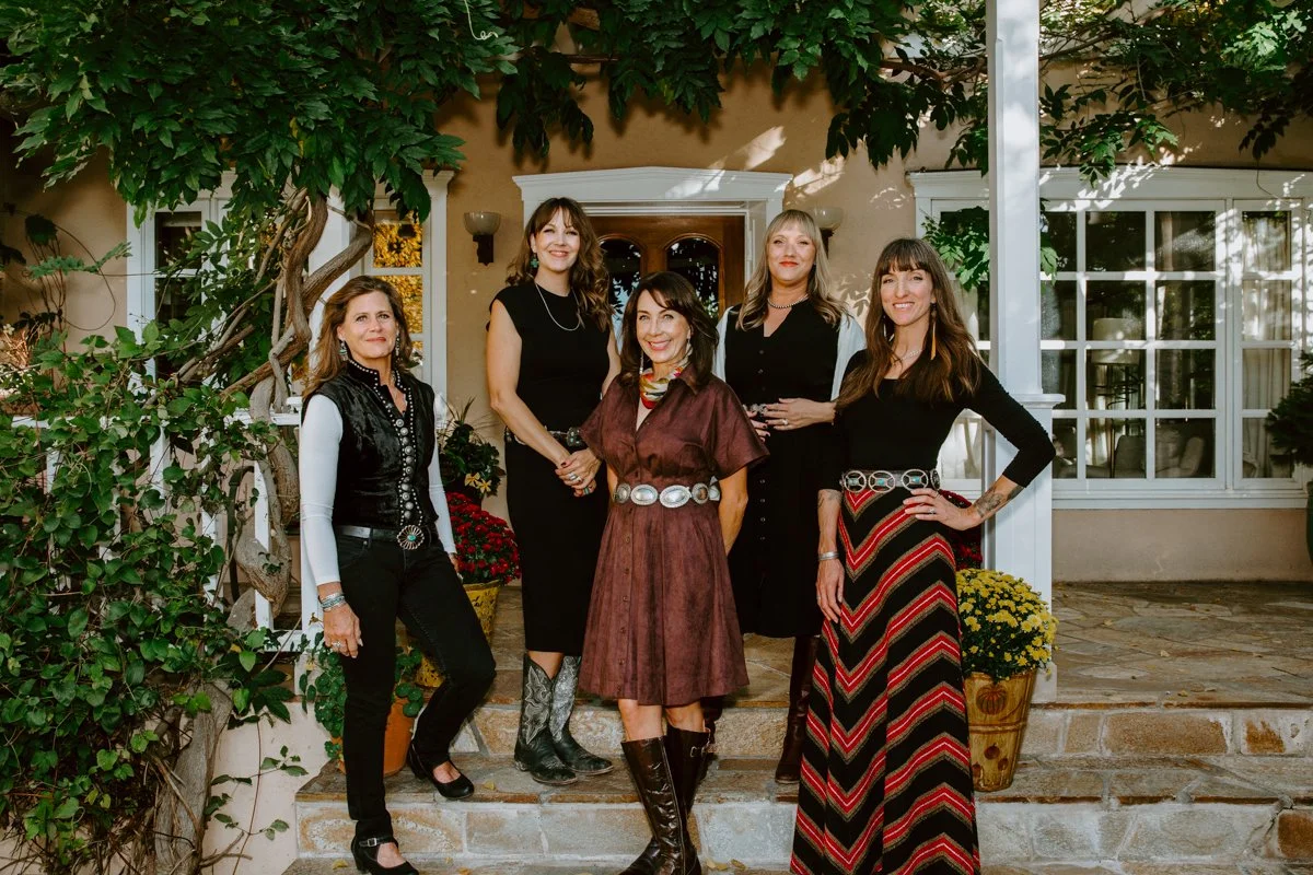 Five women posing together on the front steps of a vine-covered house.