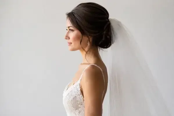 Chic oblong bridal bun with cathedral veil shown from profile angle