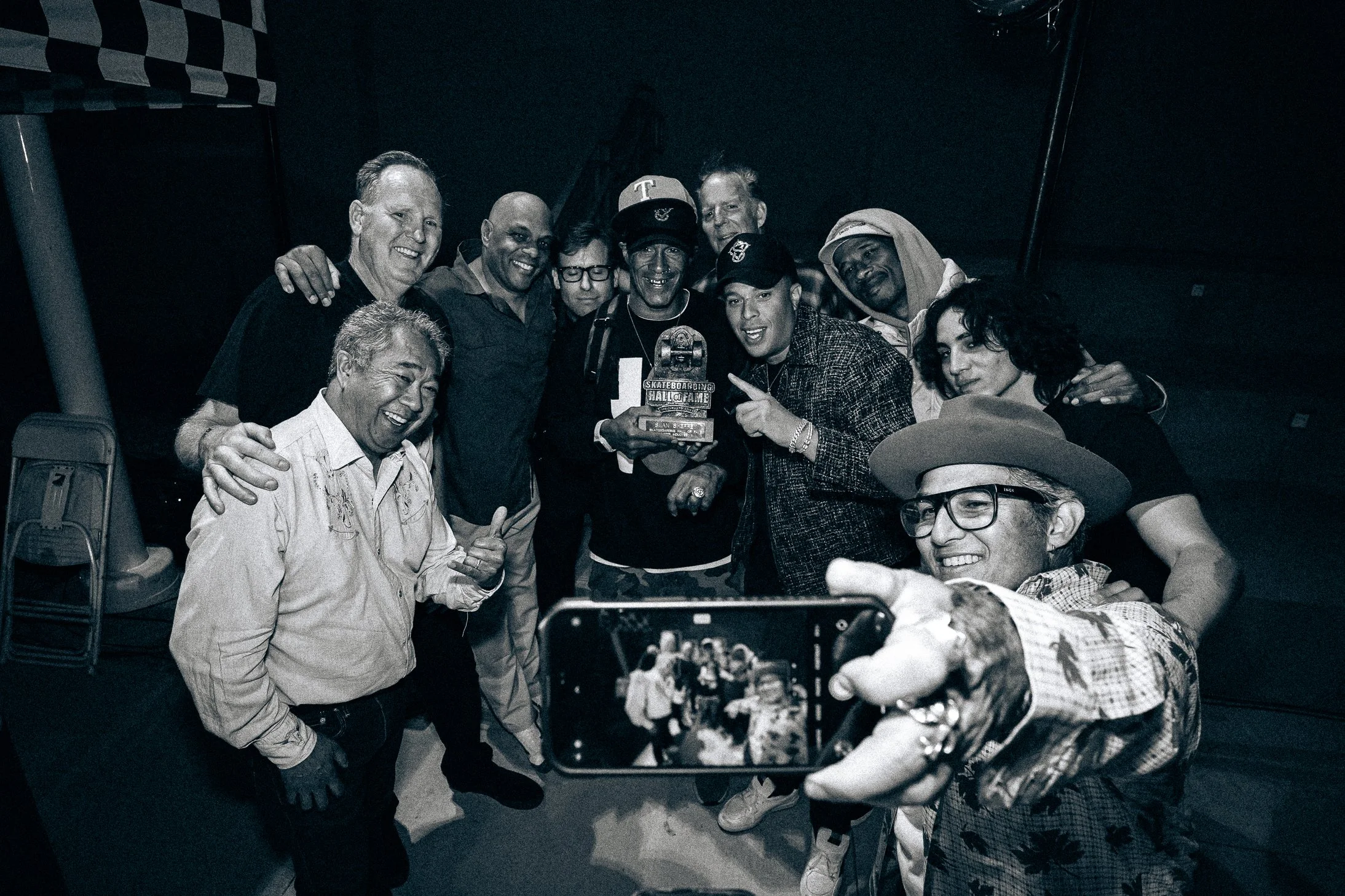 Group of people taking a photo together, one person holding an award, in a dark room.