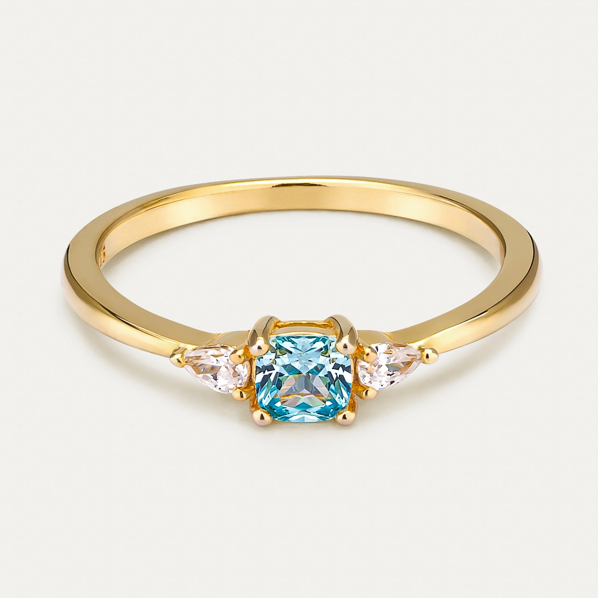 Gold ring with a blue gemstone in the center flanked by two diamonds on a white background.