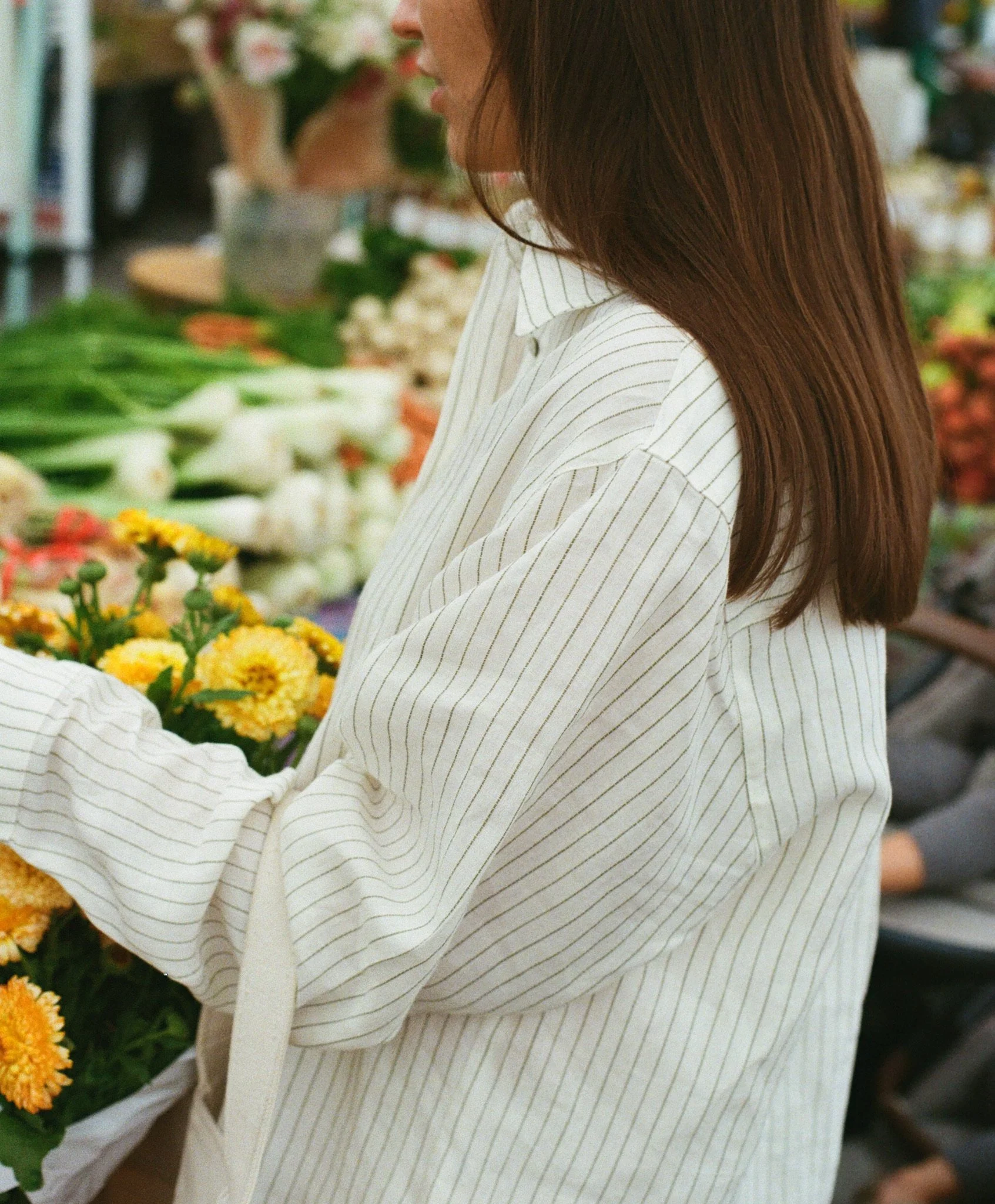 Person holding a basket of yellow flowers at a grocery store wearing Rad Habits Market Linen Shirt