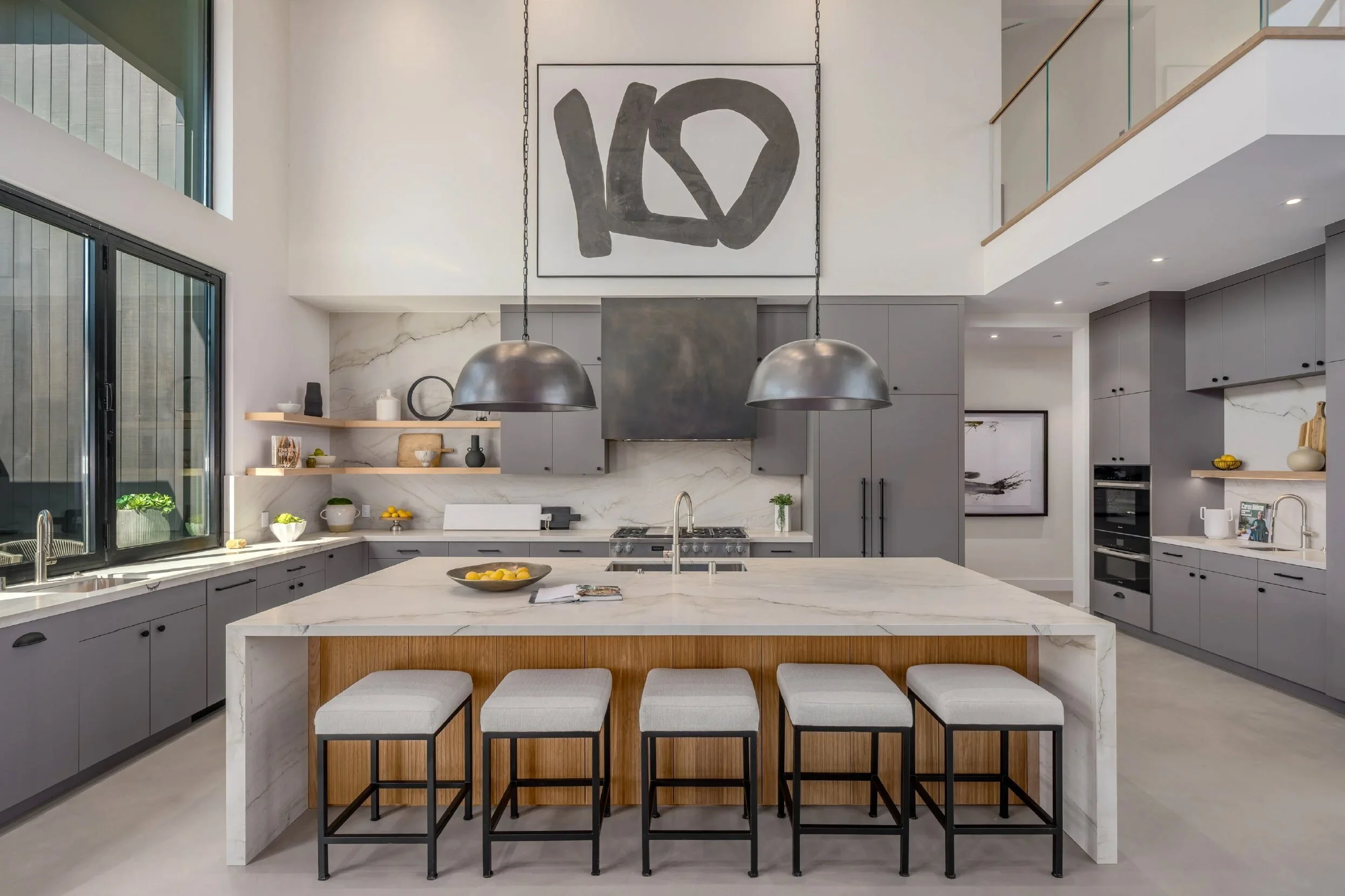 Kitchen with marble waterfall island, gray cabinetry, metal range hood, and pewter dome pendants