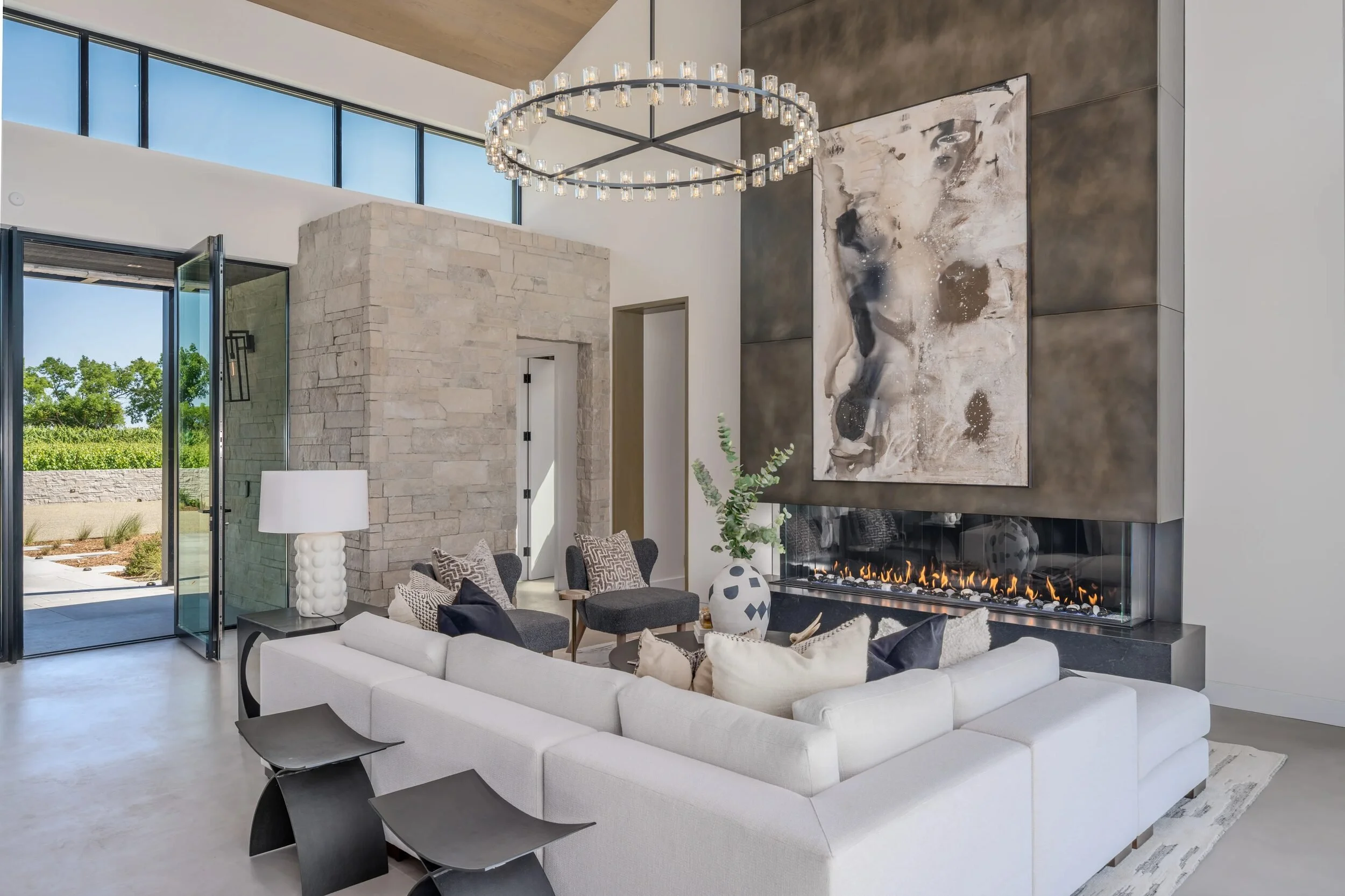 Great room with double-height ceiling, linear gas fireplace, ring chandelier, and stacked stone wall