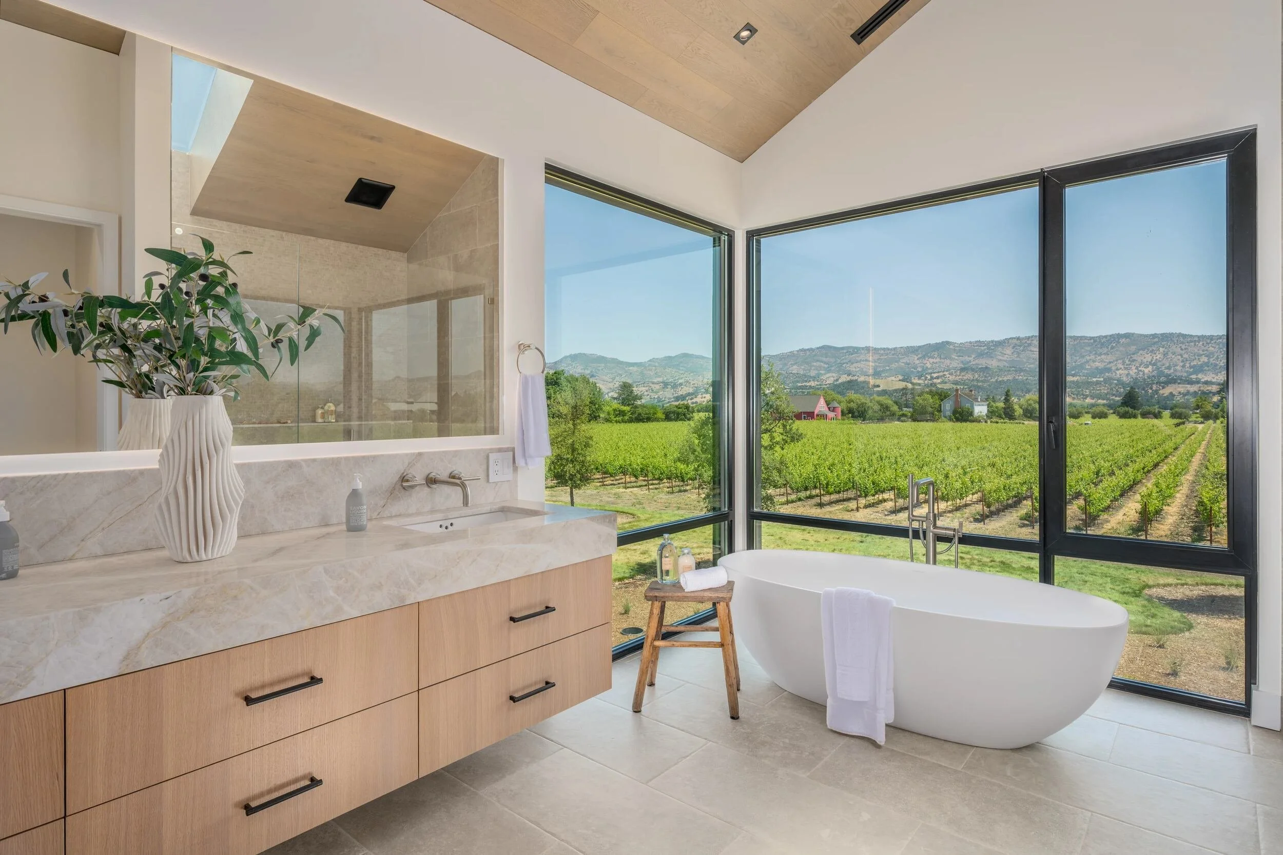 Primary bathroom with freestanding tub and floor-to-ceiling windows overlooking Napa Valley vineyards