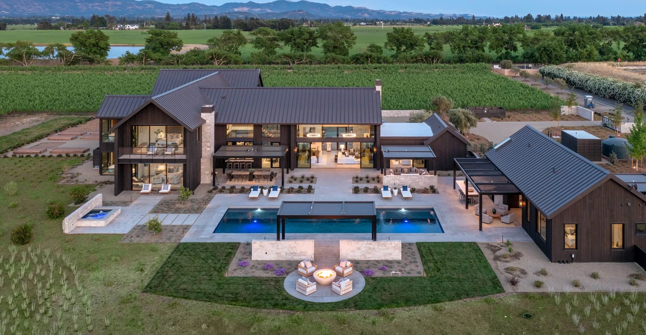 Aerial view of modern Napa Valley home with metal roof, pool, fire pit, and guest house surrounded by vineyards