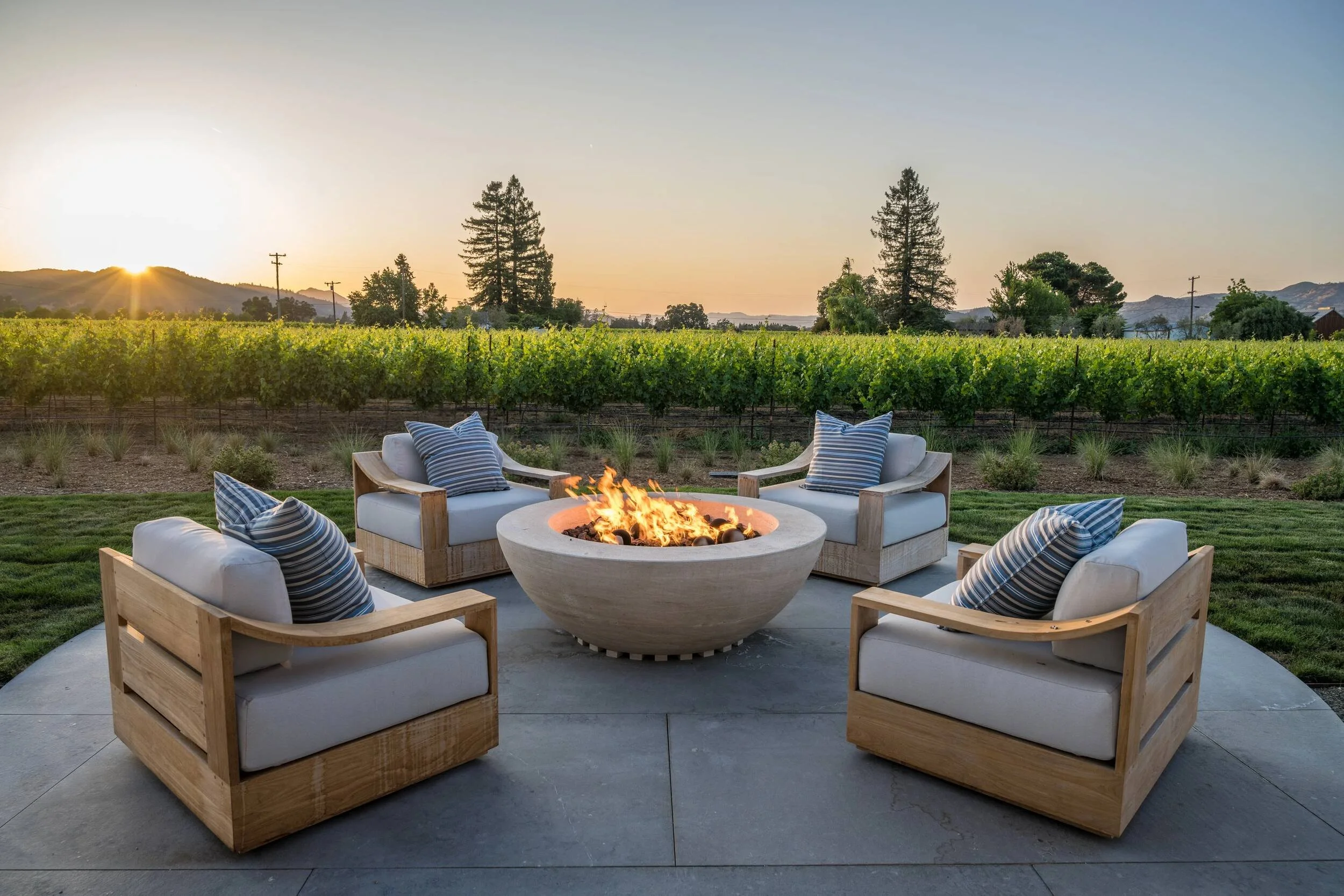 Outdoor fire pit with teak lounge chairs overlooking vineyard at sunset in Napa Valley