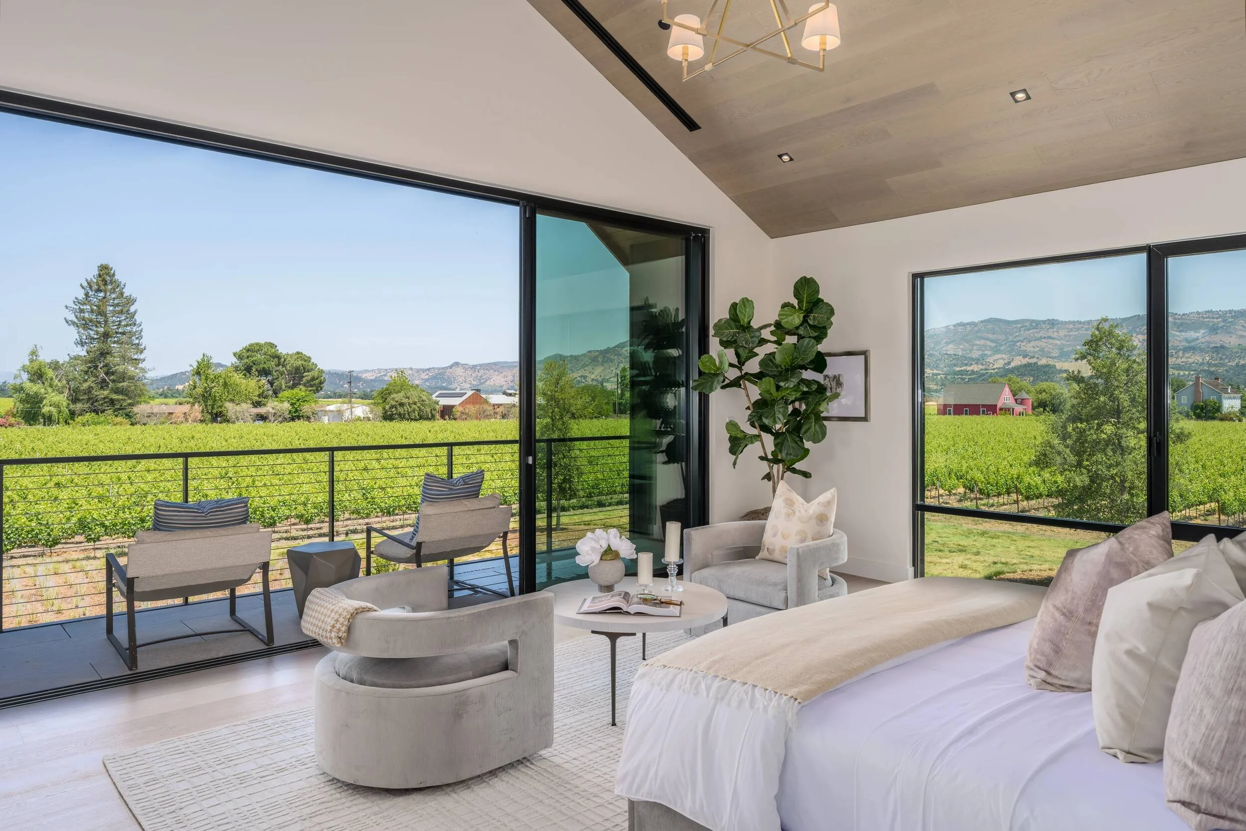 Primary bedroom with vaulted ceiling, sliding glass doors, and balcony with Napa Valley vineyard views