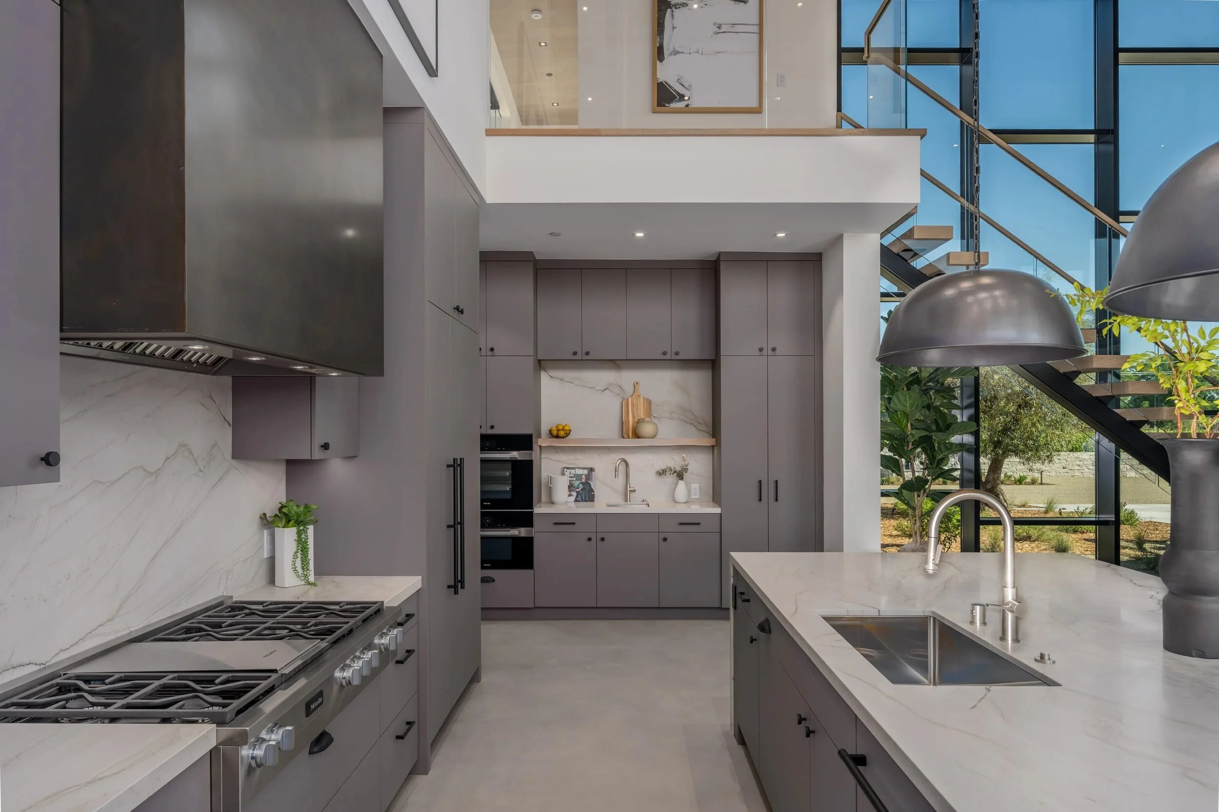 Modern kitchen with gray cabinetry, marble waterfall island, and double-height ceiling