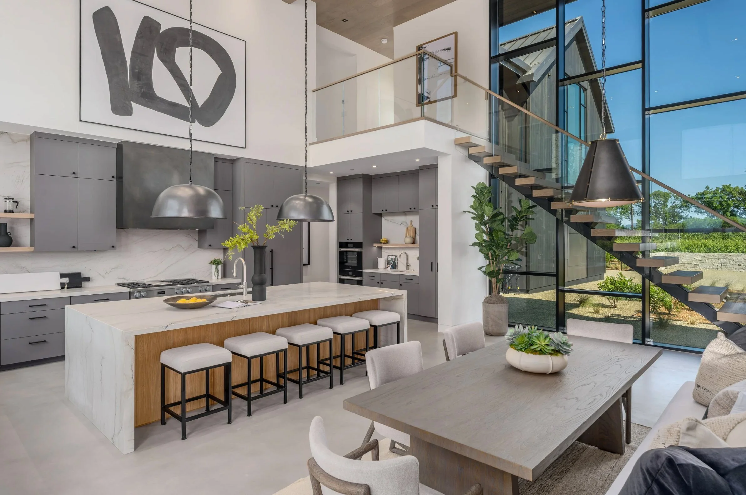Open kitchen and dining area with marble island, gray cabinetry, and floating glass staircase