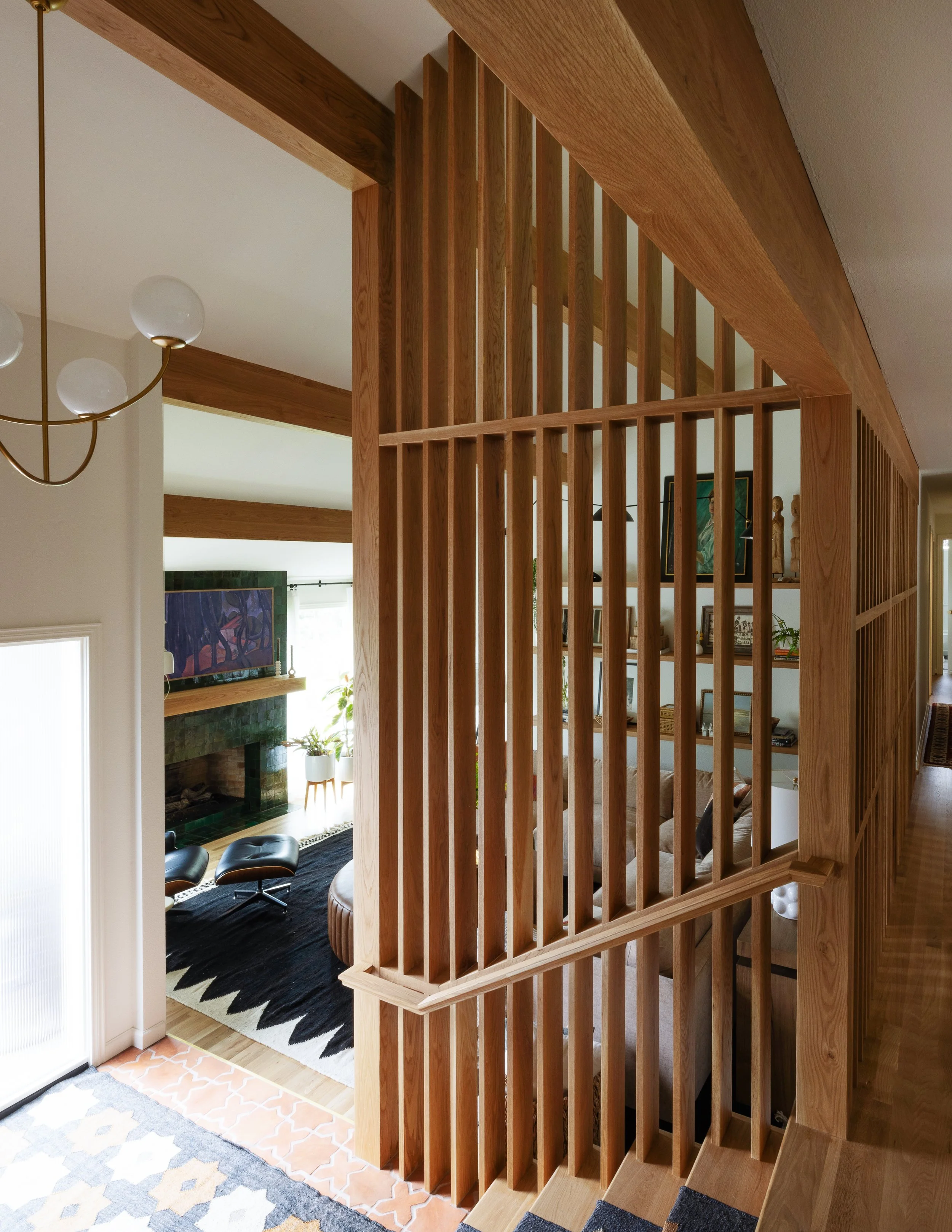 Image of a oak wood slat wall that descends down stairs to a tiled foyer