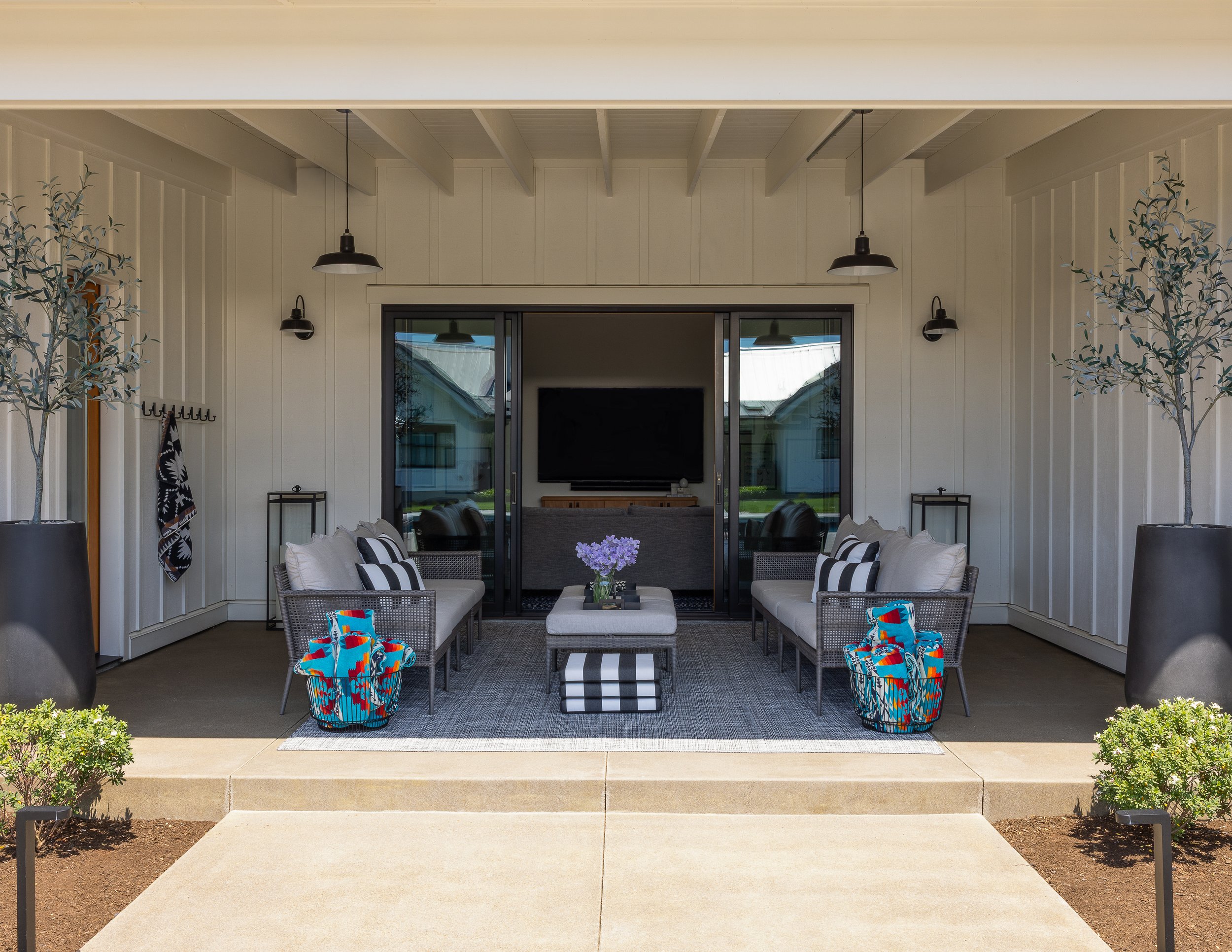 Image of a covered outdoor living space with pendant lights, olive trees in tall planters, two outdoor couches facing each other with black and white striped pillows.