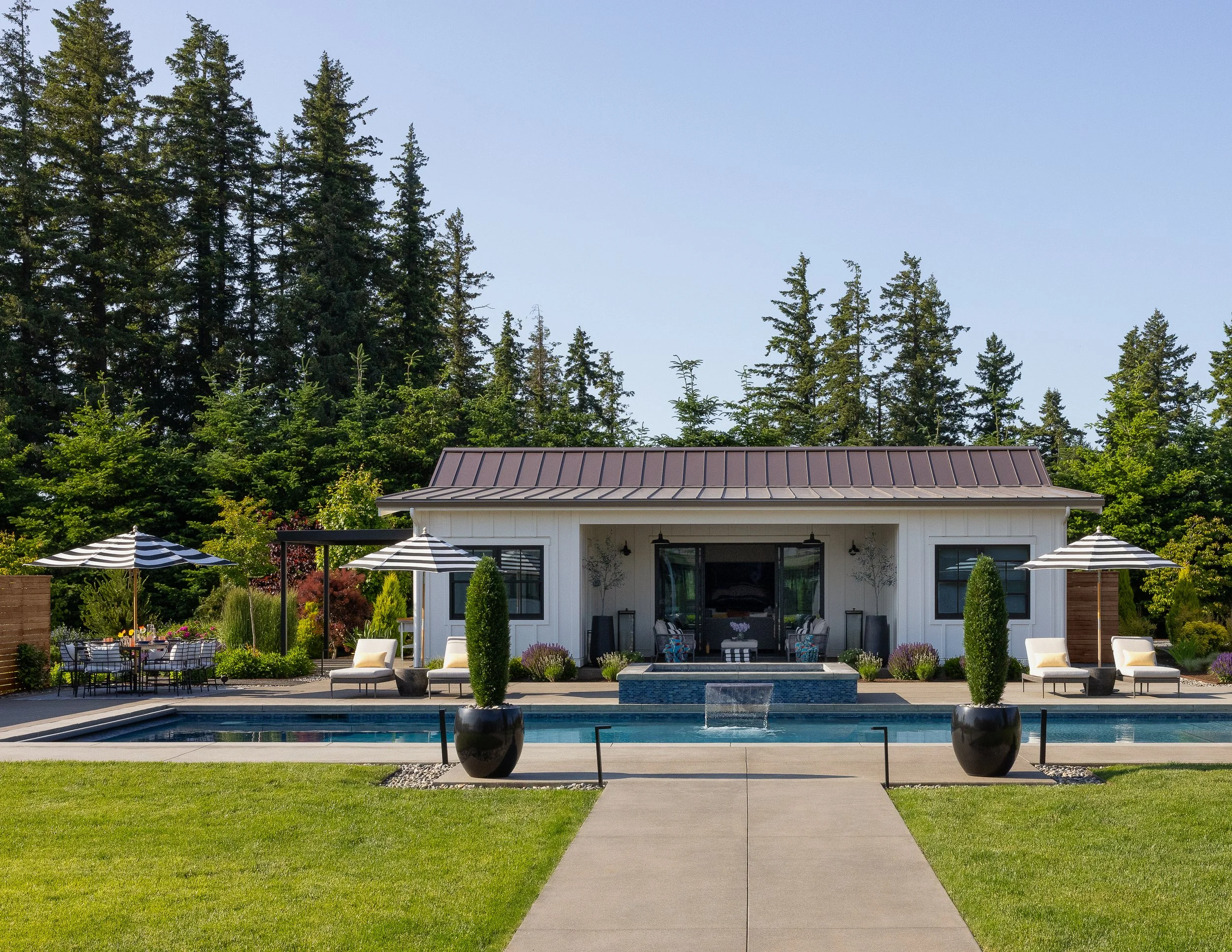 Picture of front of poolhouse, hot tub, and pool with Italian Cypress trees in pots.