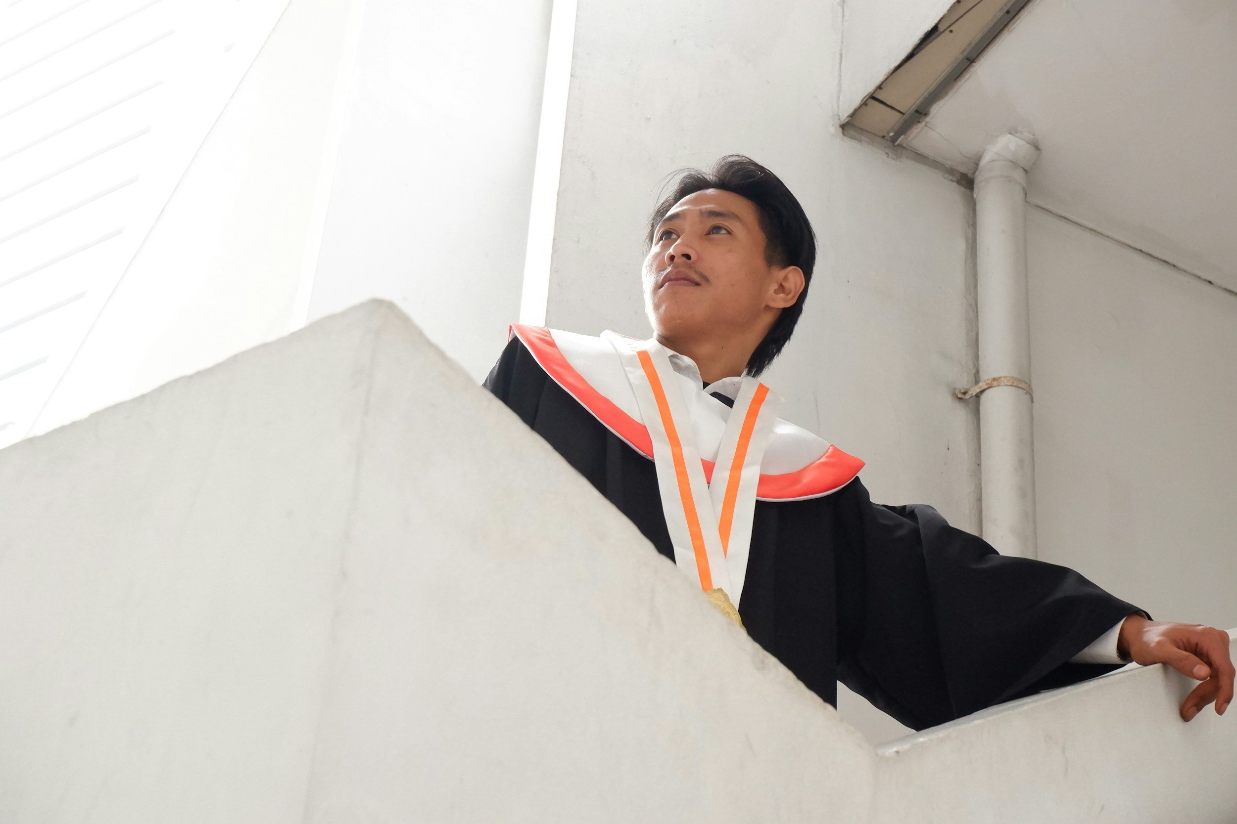 A young college graduate in a cap and gown looking up hopefully