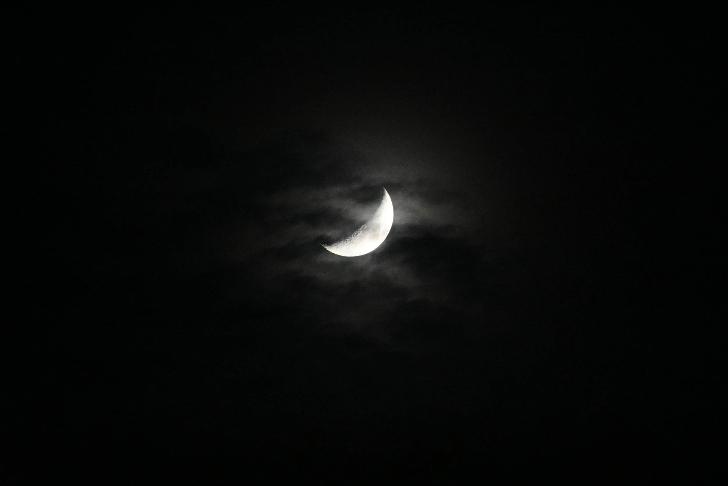 The moon visible in a dark night sky with some clouds around it.