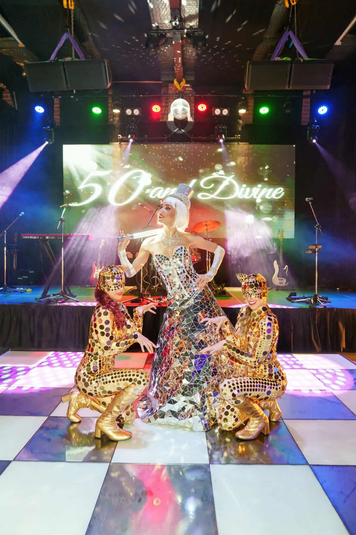 Mirrorball performer mid-twirl on dance floor while dancers strike playful feline poses around her.