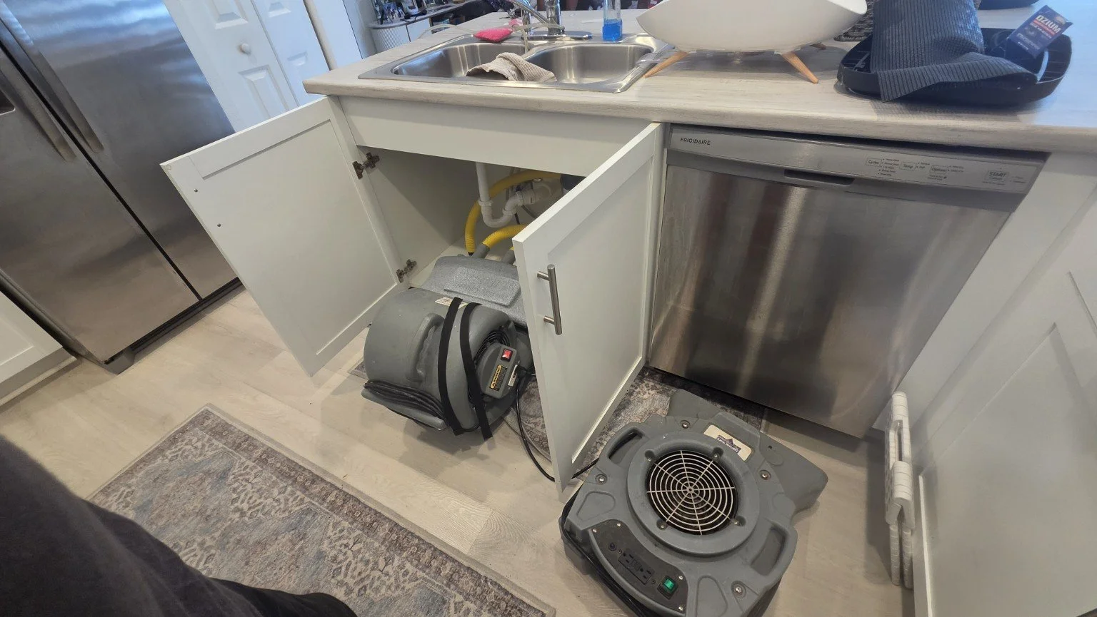 Under-sink drying setup with an air mover beside the dishwasher.