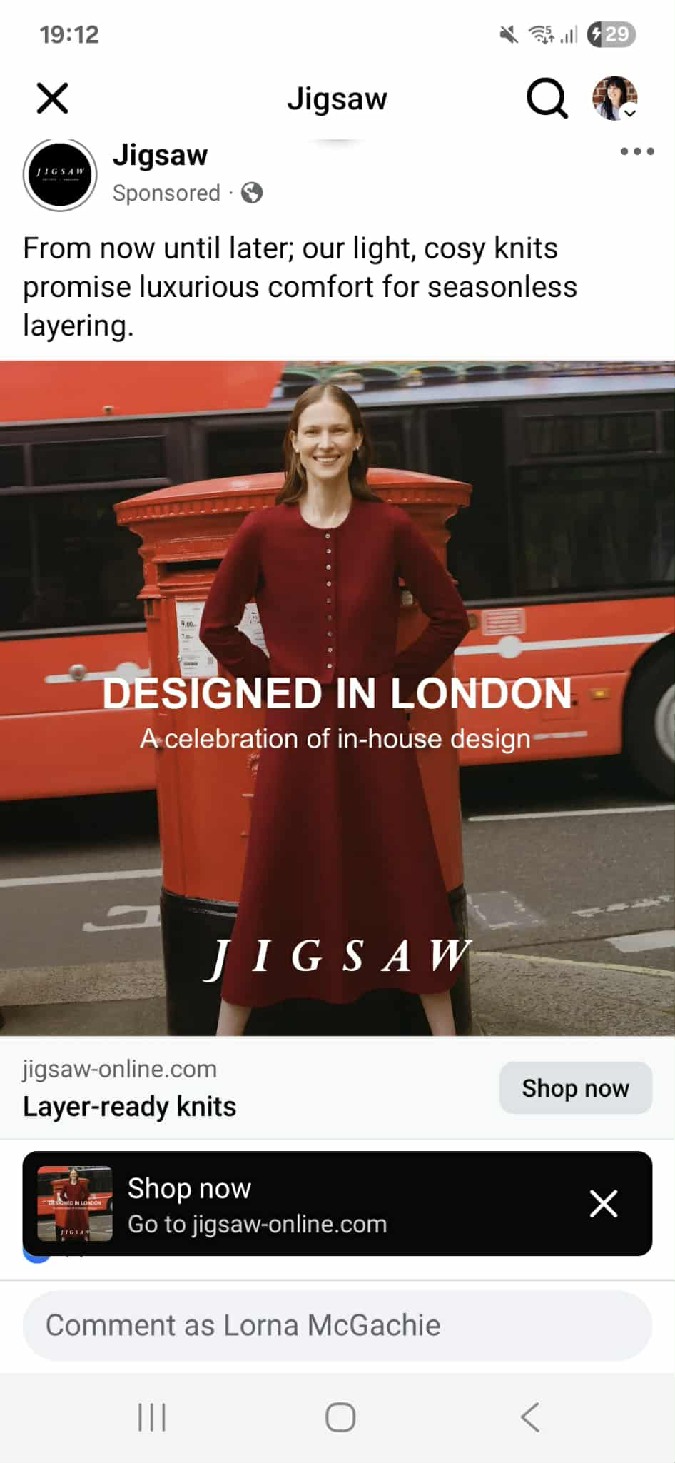 A female model standing in front of a classic red British post box wearing a red co-ord; a long-sleeve textured cardigan cardigan teamed with a red midi length skirt