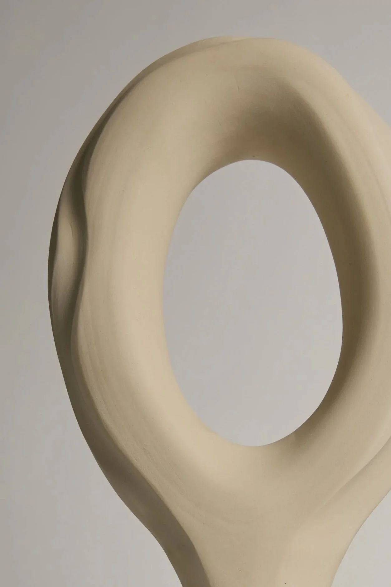 Close-up image of a cream-colored ceramic sculpture resembling a modern abstract shape with smooth curves and a hole in the center.