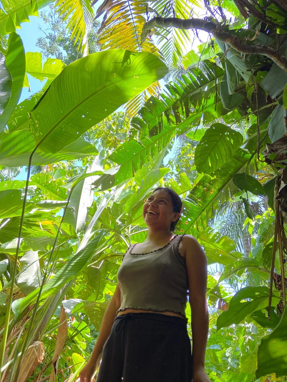 Jeune femme avec des cheveux noirs, portant un t-shirt à rayures rouges et blanches, en train de parler en face de l'appareil photo, avec un mur jaune en arrière-plan.